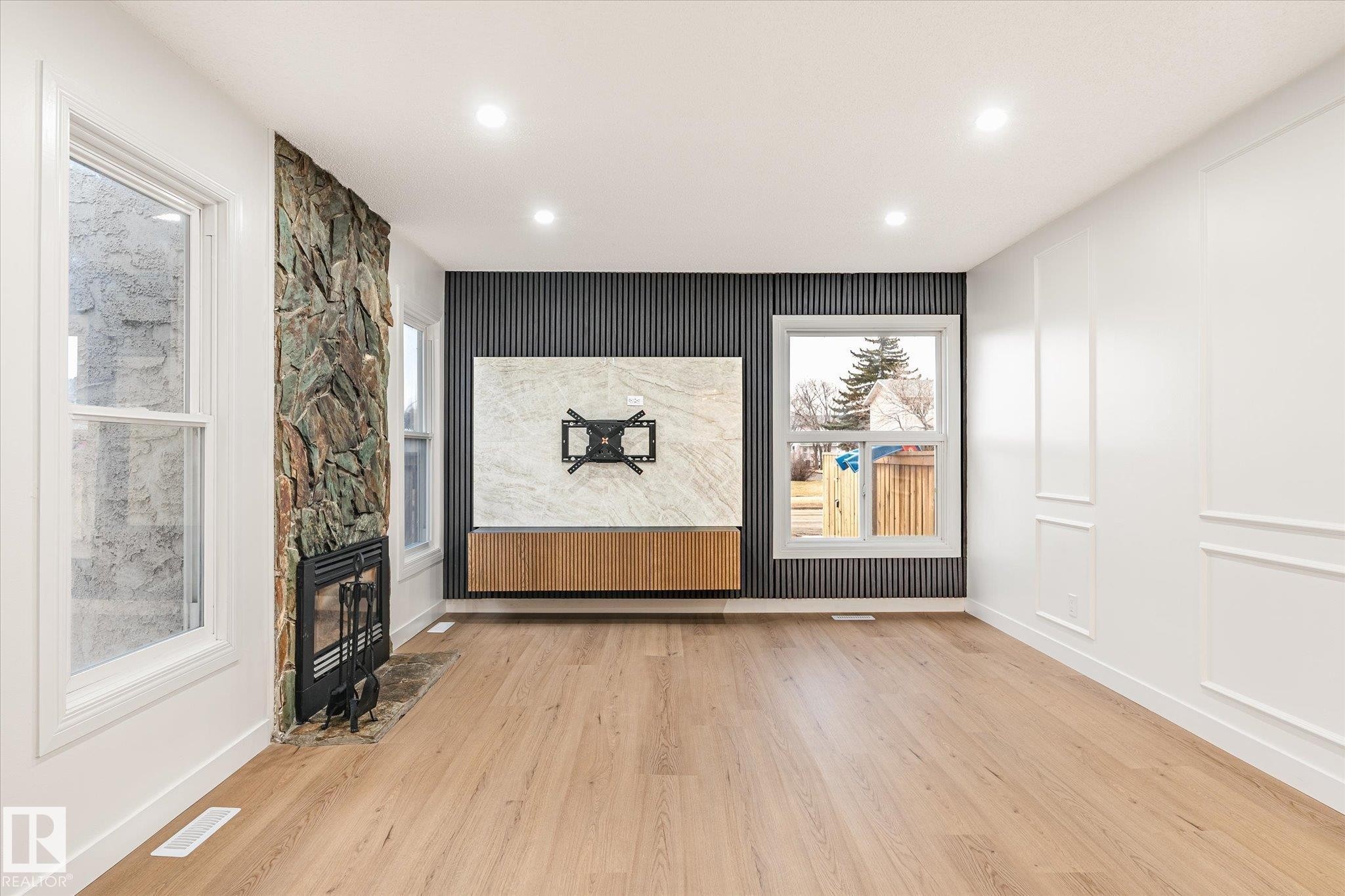 Living area featuring wood flooring, a stone accent wall with a fireplace, recessed lighting, and white paneled walls - 6540 184 Street, Edmonton, AB - Indoor Photo Showing Other Room With Fireplace