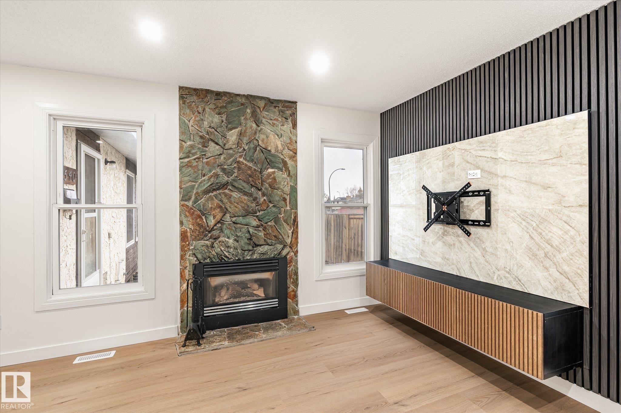 Living room featuring hardwood floors, a natural stone fireplace, and two windows - 6540 184 Street, Edmonton, AB - Indoor Photo Showing Living Room With Fireplace