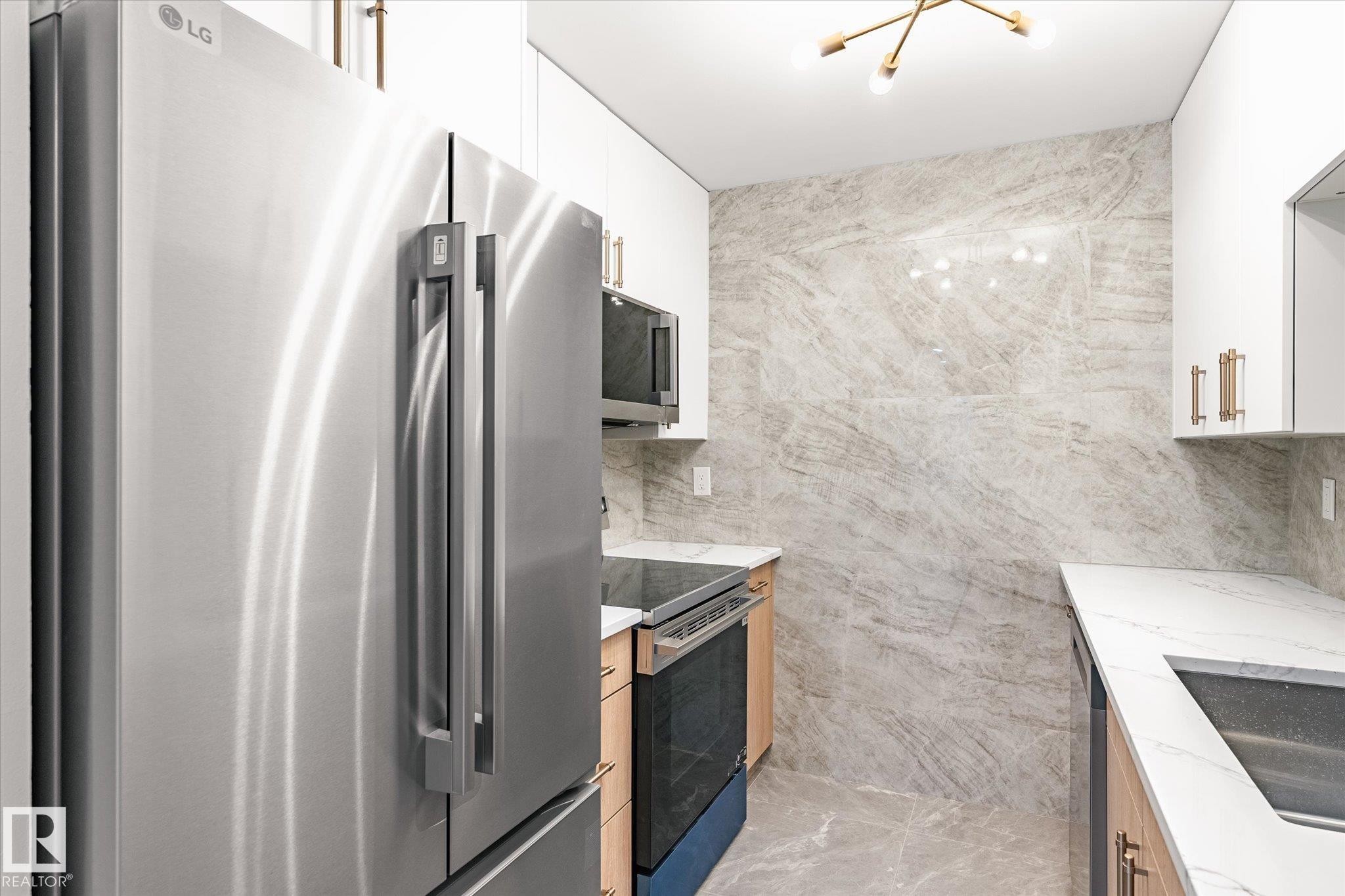 The kitchen features stainless steel appliances, white cabinetry, light wood lower cabinets, and stone-look tile flooring and walls - 6540 184 Street, Edmonton, AB - Indoor Photo Showing Kitchen With Double Sink With Upgraded Kitchen