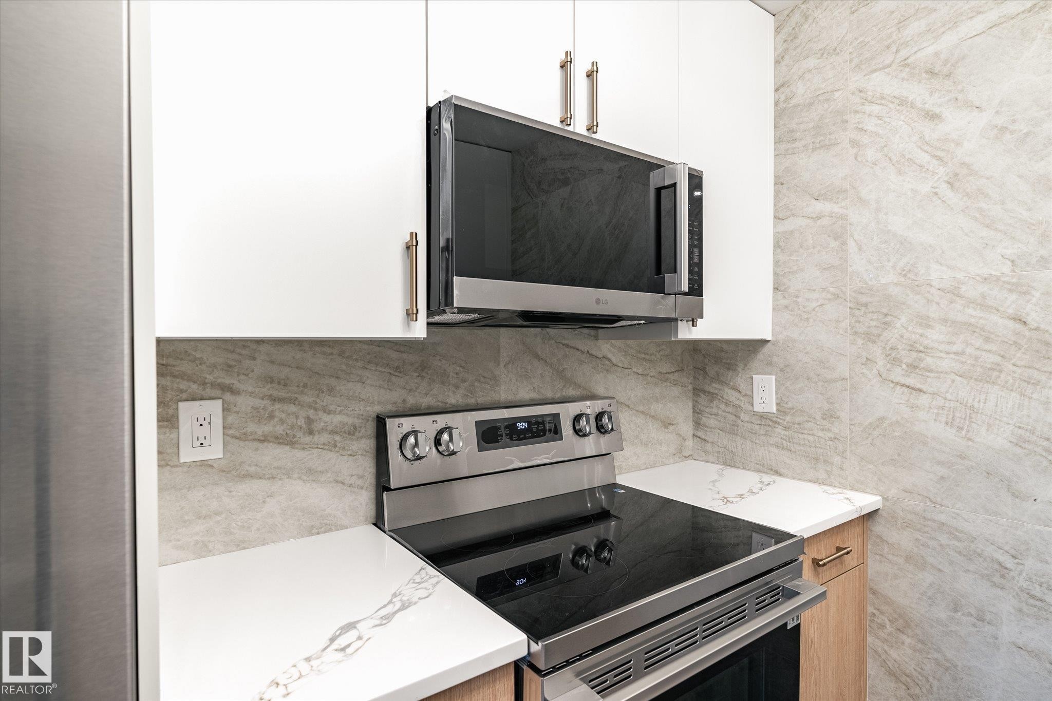 Well-appointed kitchen featuring white upper cabinetry, stainless steel appliances, white countertops with natural veining, and a stone-tiled backsplash - 6540 184 Street, Edmonton, AB - Indoor Photo Showing Kitchen