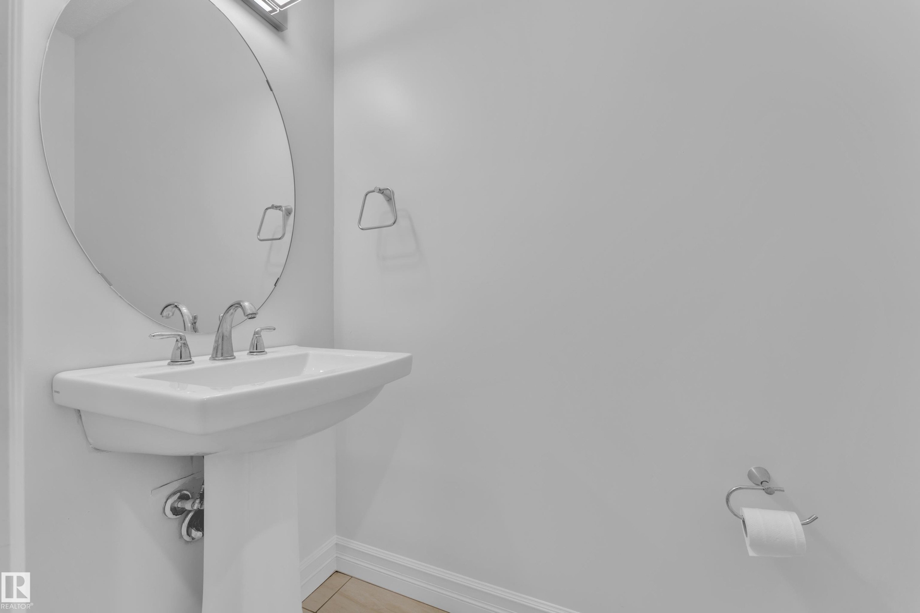 Pedestal sink with chrome fixtures and an oval mirror, complemented by a wall-mounted light fixture - 3235 13 Avenue, Edmonton, AB - Indoor Photo Showing Bathroom