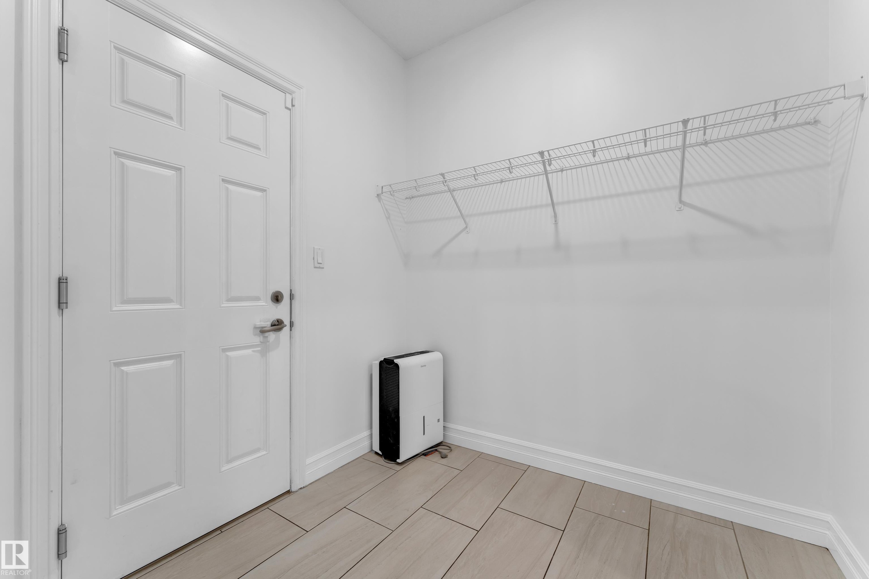 This utility space features a white paneled door, light-colored tiled flooring, and a white wire shelving unit mounted on the wall - 3235 13 Avenue, Edmonton, AB - Indoor