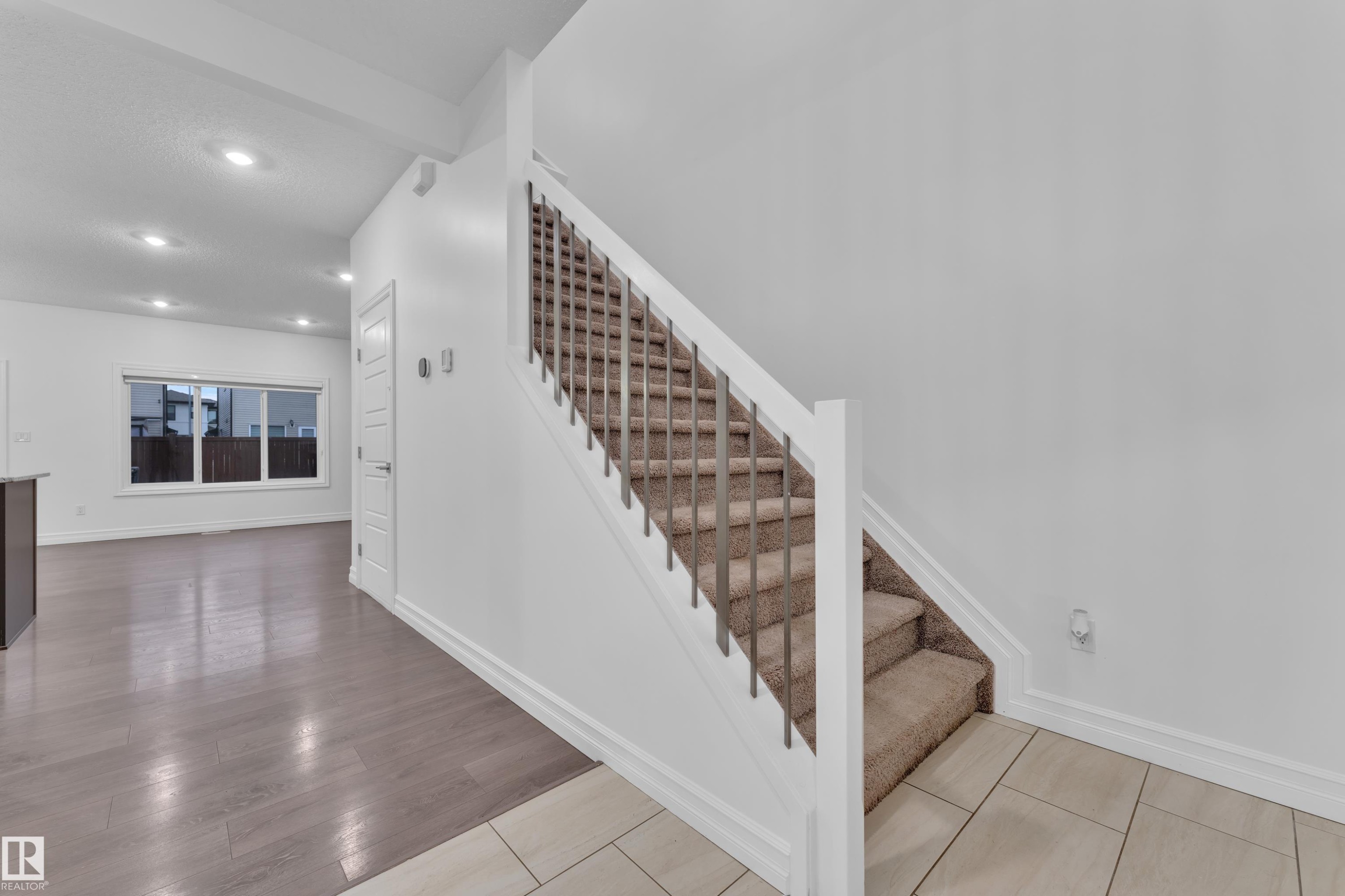 Entryway featuring a carpeted staircase with modern railings, tiled flooring, and a view of the main living area with hardwood floors and a large window - 3235 13 Avenue, Edmonton, AB - Indoor Photo Showing Other Room