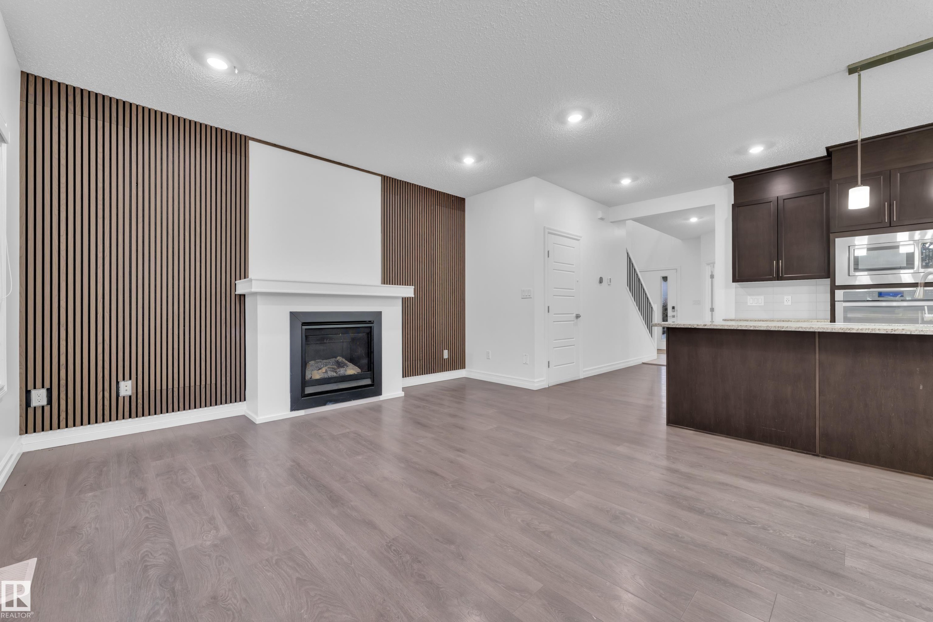 The property features a spacious living area with light-colored flooring, a modern fireplace with a white mantel, and a striking accent wall with vertical wood paneling - 3235 13 Avenue, Edmonton, AB - Indoor With Fireplace