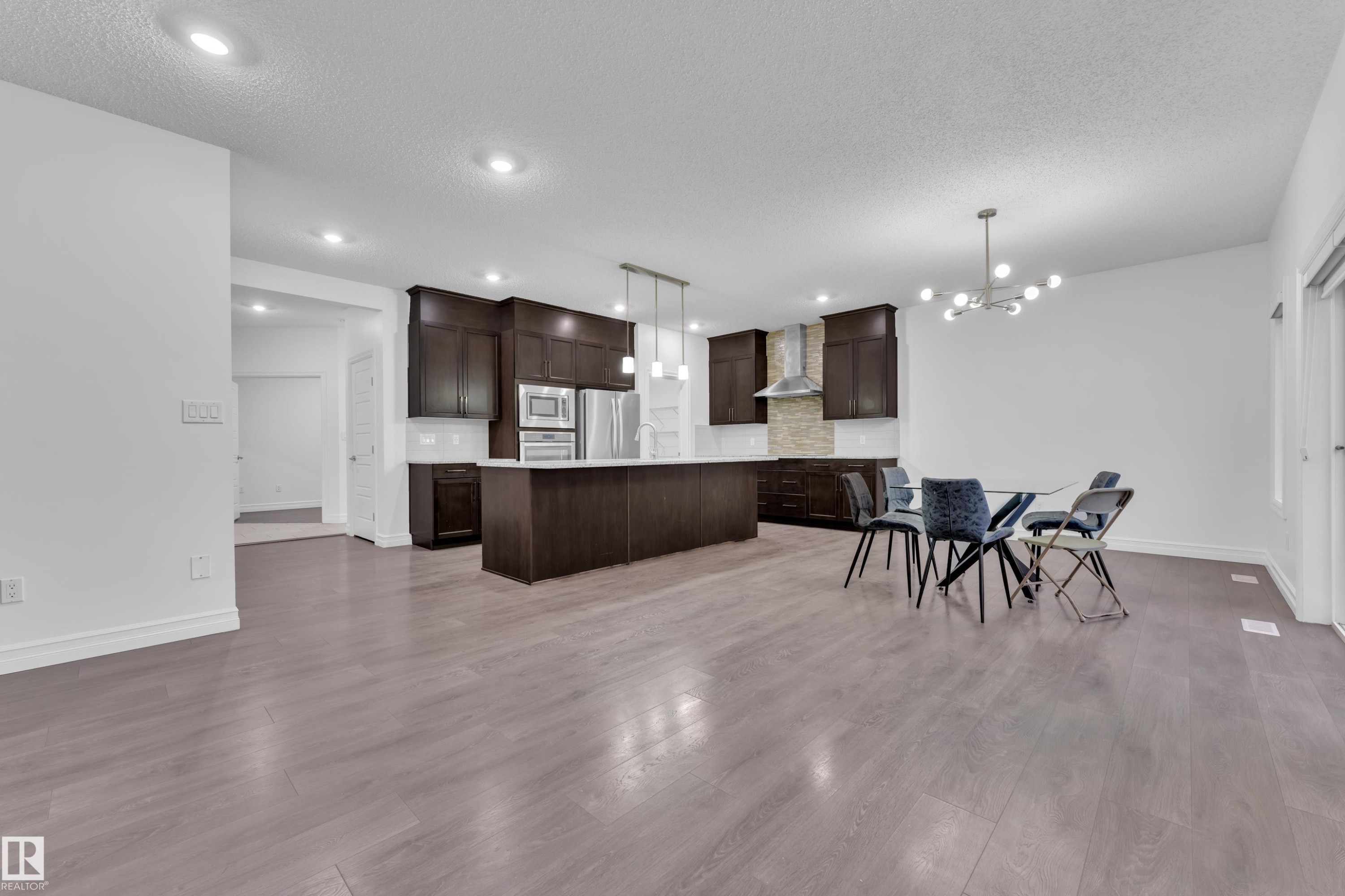 Open concept kitchen and dining area featuring dark wood cabinetry, stainless steel appliances, a kitchen island, and light wood flooring - 3235 13 Avenue, Edmonton, AB - Indoor