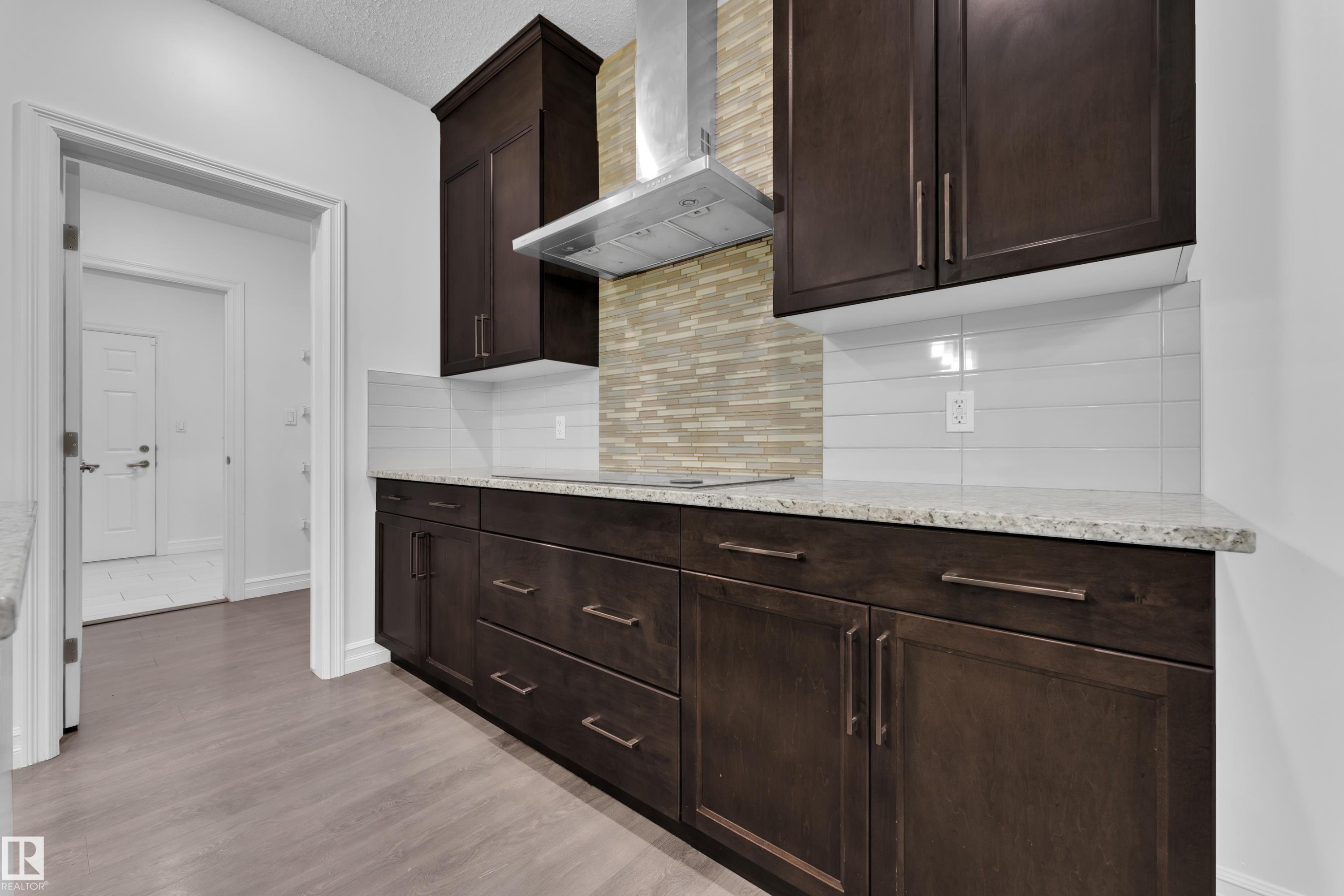 The kitchen features dark wood cabinetry, light speckled countertops, and a subway tile backsplash - 3235 13 Avenue, Edmonton, AB - Indoor