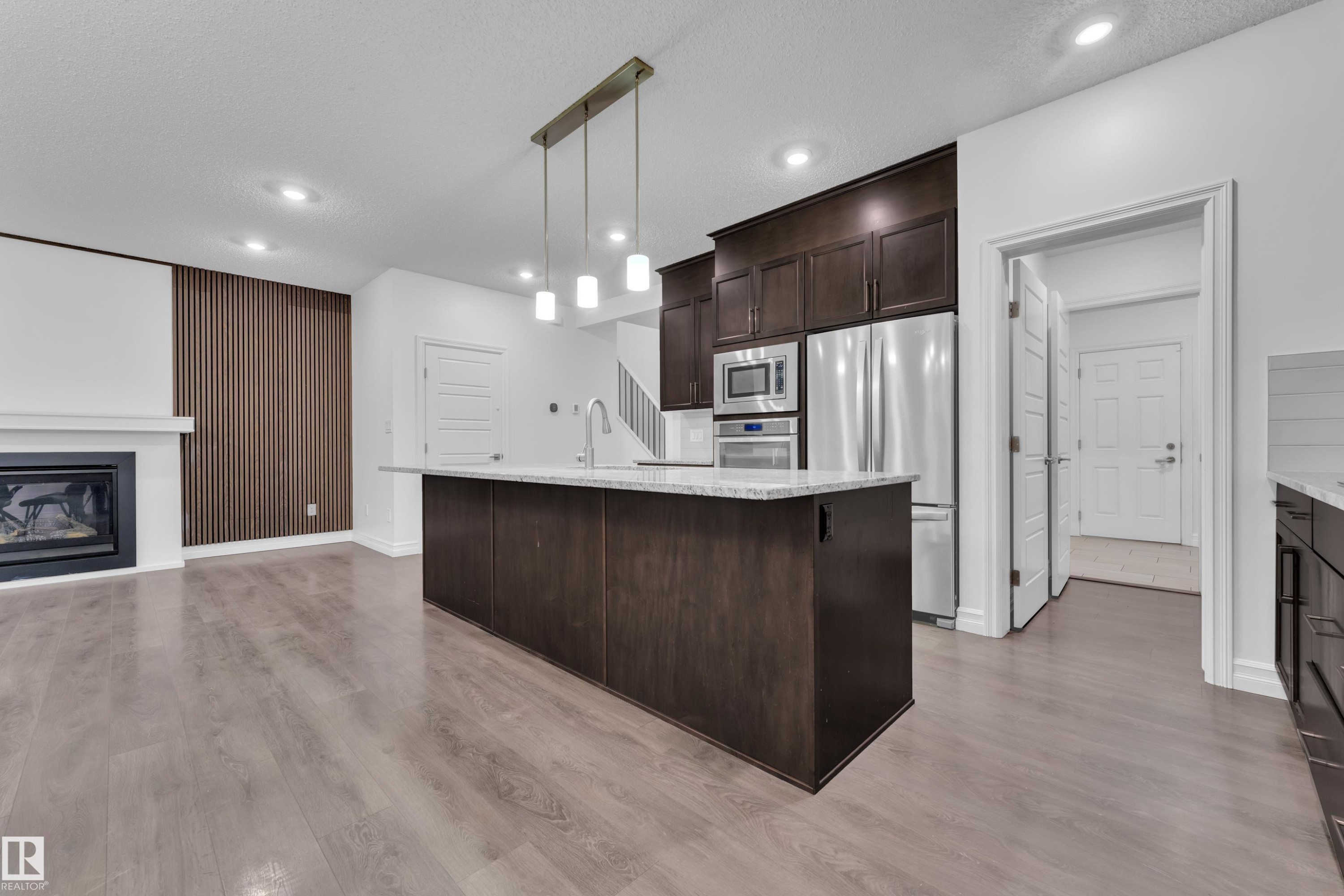 Open concept living space featuring a kitchen island with a light-colored countertop, stainless steel appliances, and a fireplace with a white mantel - 3235 13 Avenue, Edmonton, AB - Indoor Photo Showing Kitchen With Fireplace With Upgraded Kitchen
