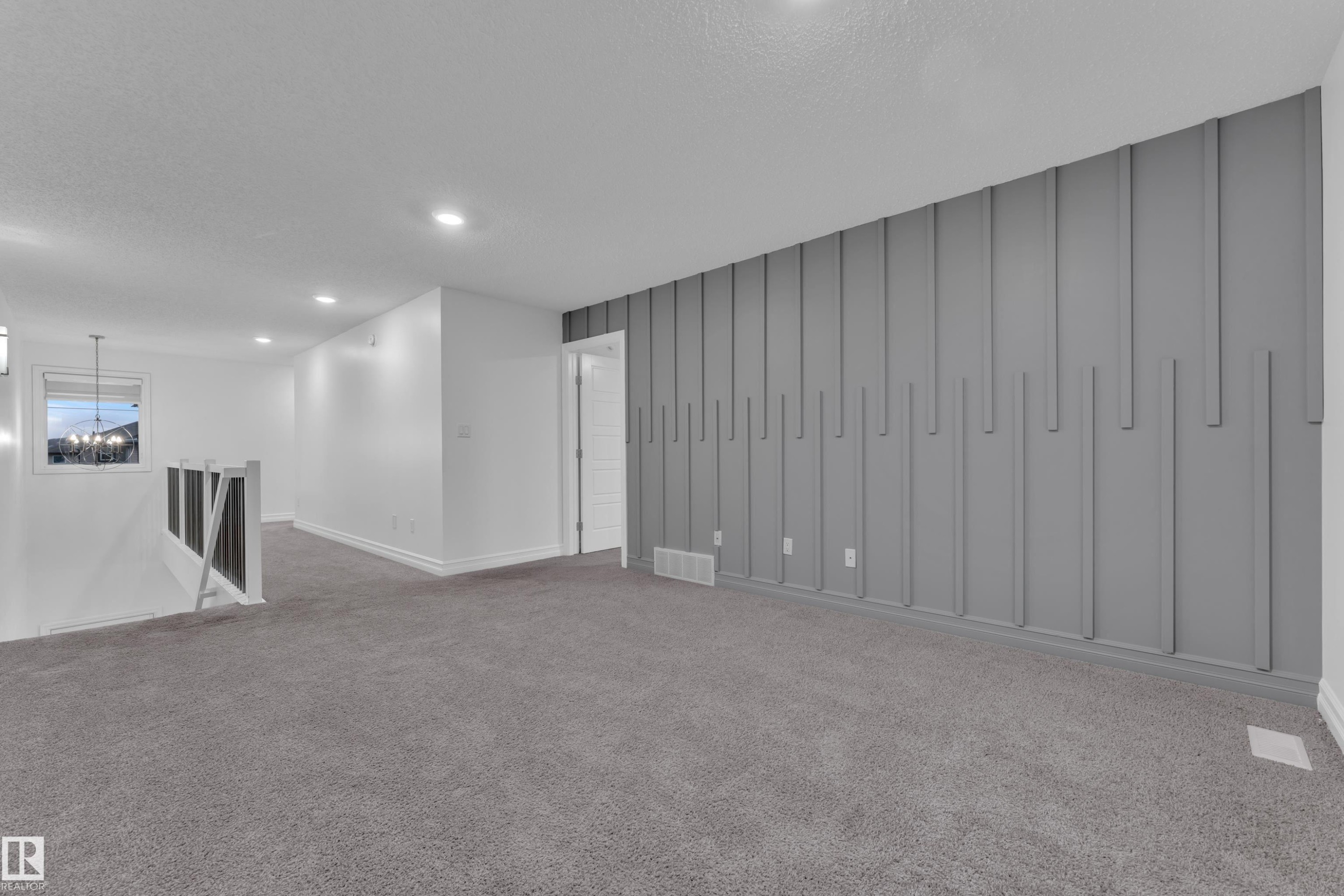 The property features a spacious room with grey carpet flooring and a distinctive accent wall with vertical paneling - 3235 13 Avenue, Edmonton, AB - Indoor Photo Showing Other Room