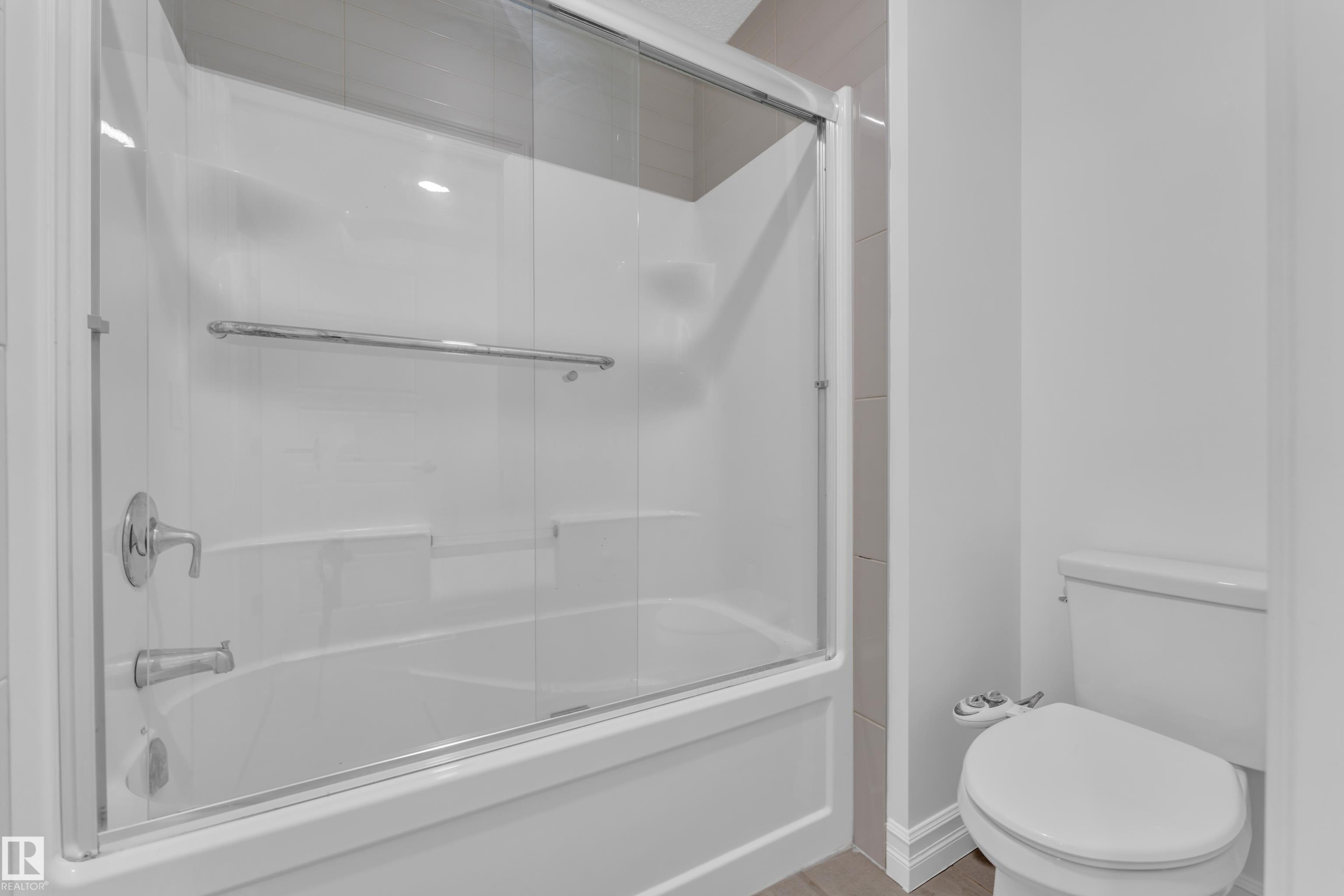 Bathroom featuring a bathtub with a clear glass sliding shower door and a toilet - 3235 13 Avenue, Edmonton, AB - Indoor Photo Showing Bathroom