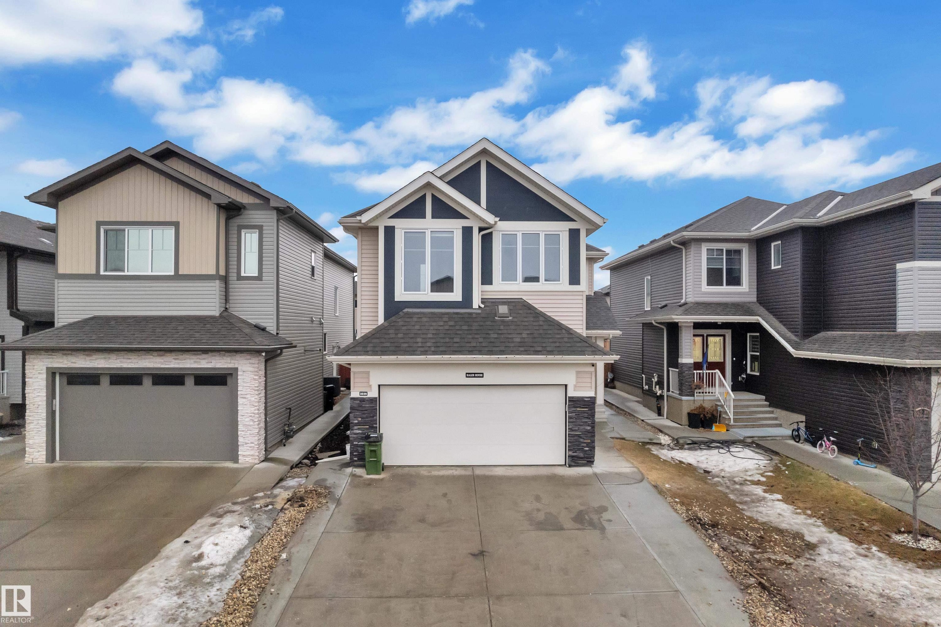 The property features a dark grey roof, a two-car garage with a white door, and a light-colored exterior with dark trim - 3235 13 Avenue, Edmonton, AB - Outdoor With Facade