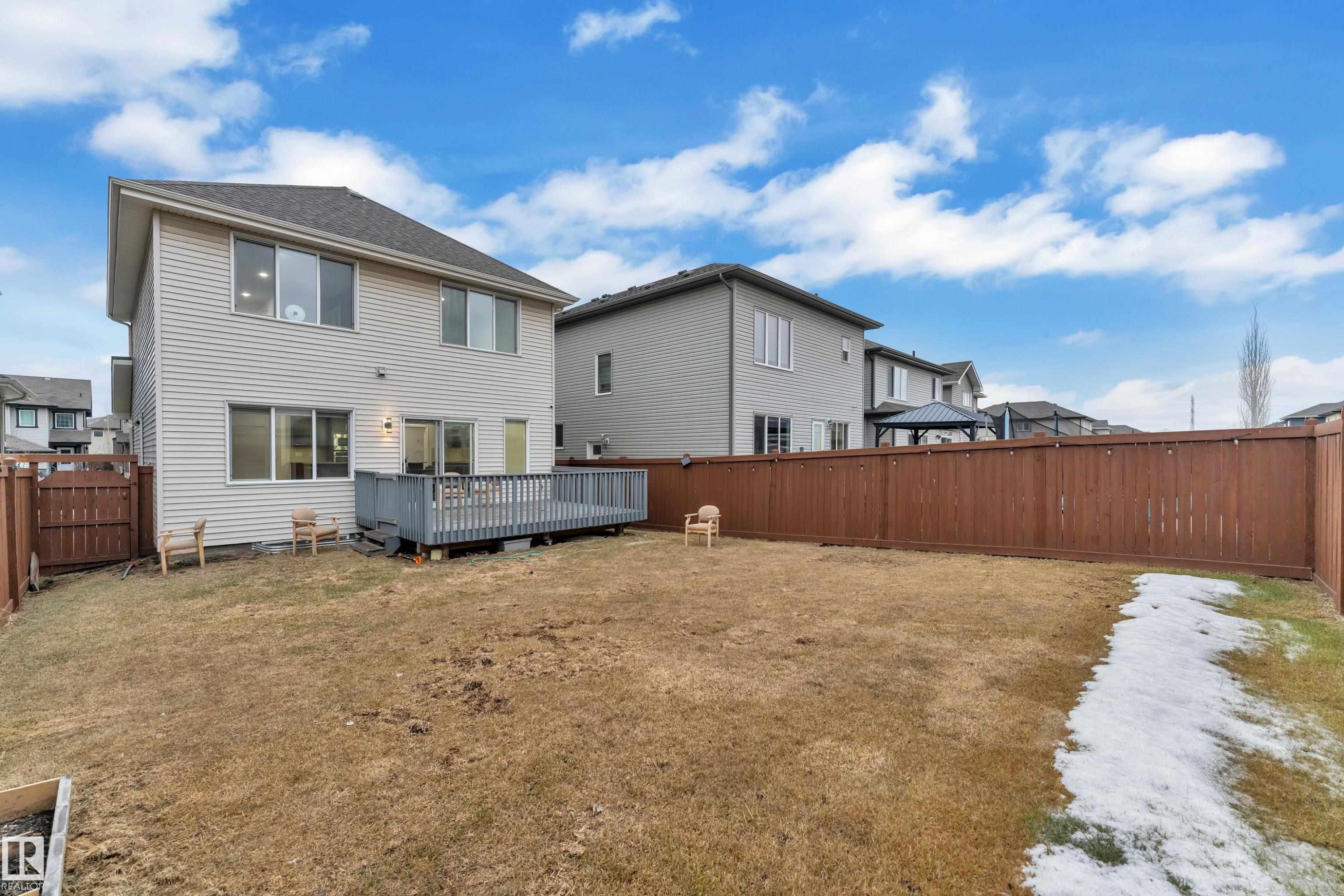 The property features a fenced backyard with a wooden deck, a spacious lawn, and a two-story exterior with horizontal siding - 3235 13 Avenue, Edmonton, AB - Outdoor With Deck Patio Veranda With Exterior