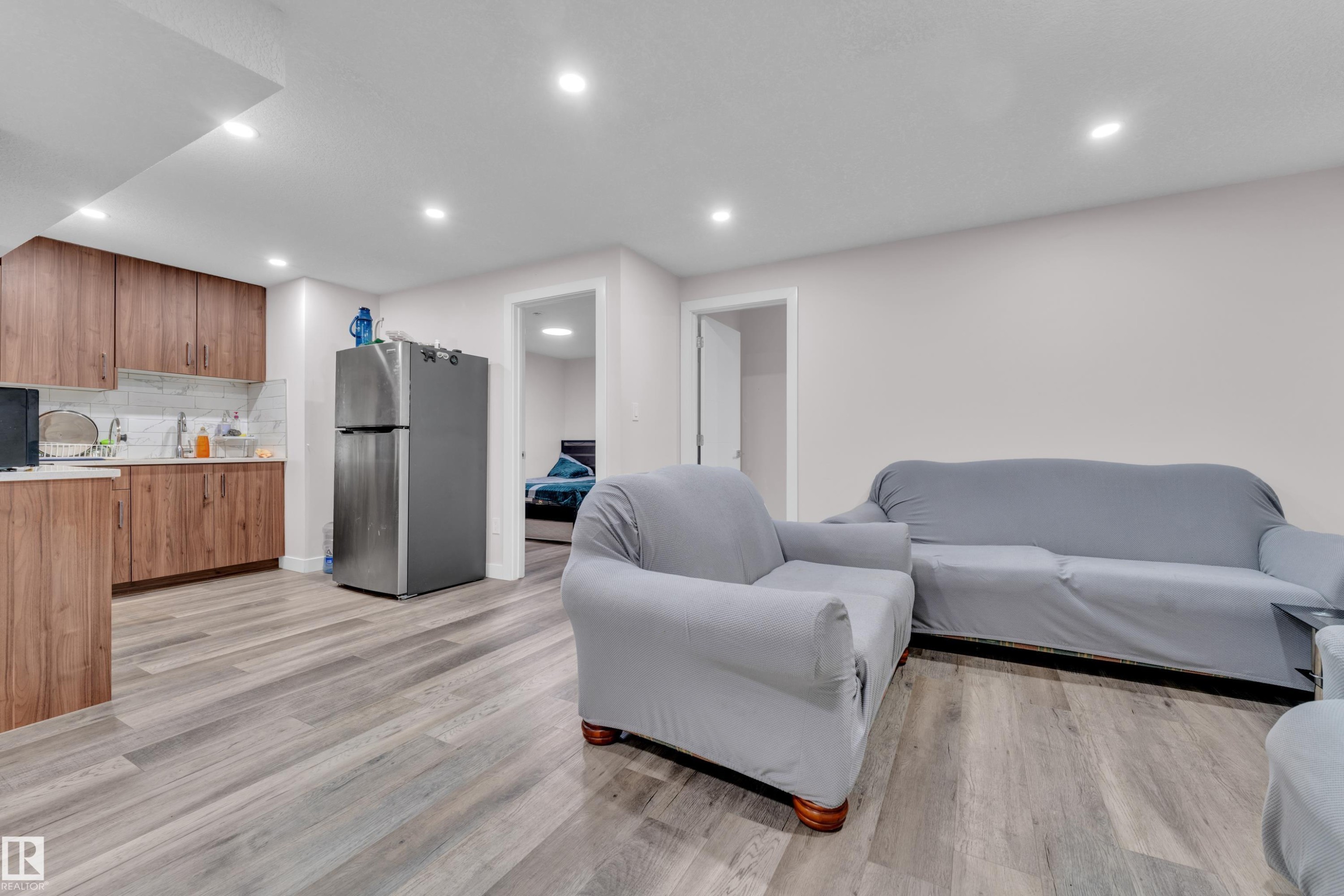 The property features a kitchen area with wood cabinetry, a stainless steel refrigerator, and a light-colored backsplash - 3235 13 Avenue, Edmonton, AB - Indoor