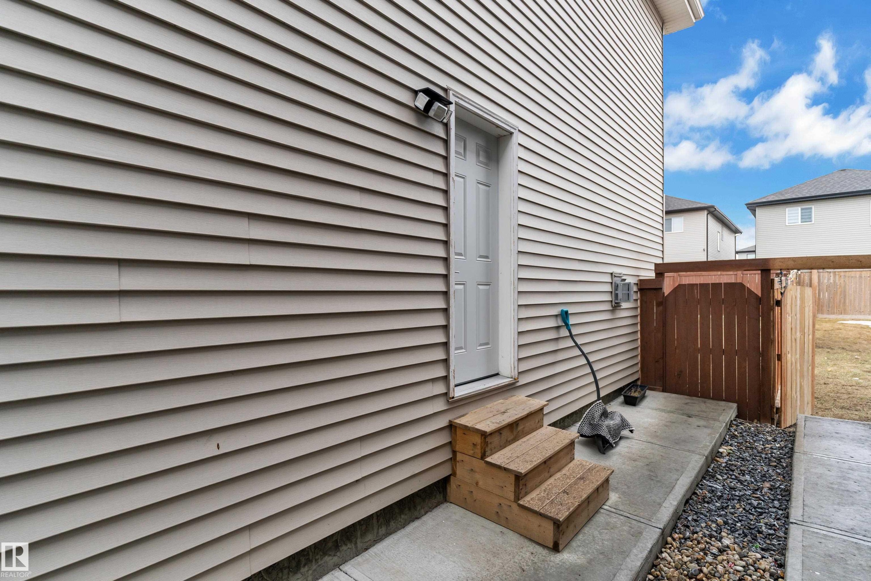 The property features neutral-toned horizontal siding and a white side door with wooden steps - 3235 13 Avenue, Edmonton, AB - Outdoor