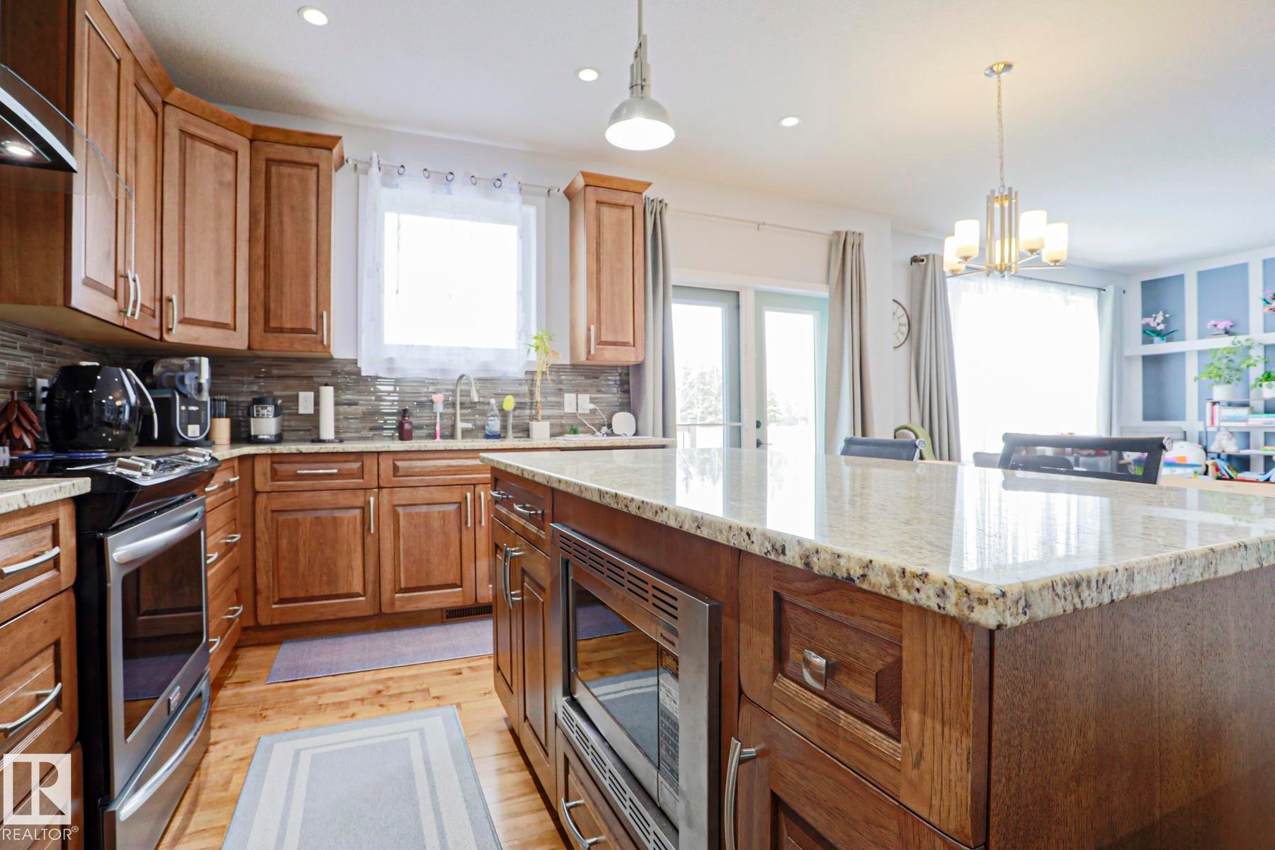 The kitchen features wooden cabinetry, stainless steel appliances, a tile backsplash, and light-colored granite countertops - 18 Enchanted Way, St. Albert, AB