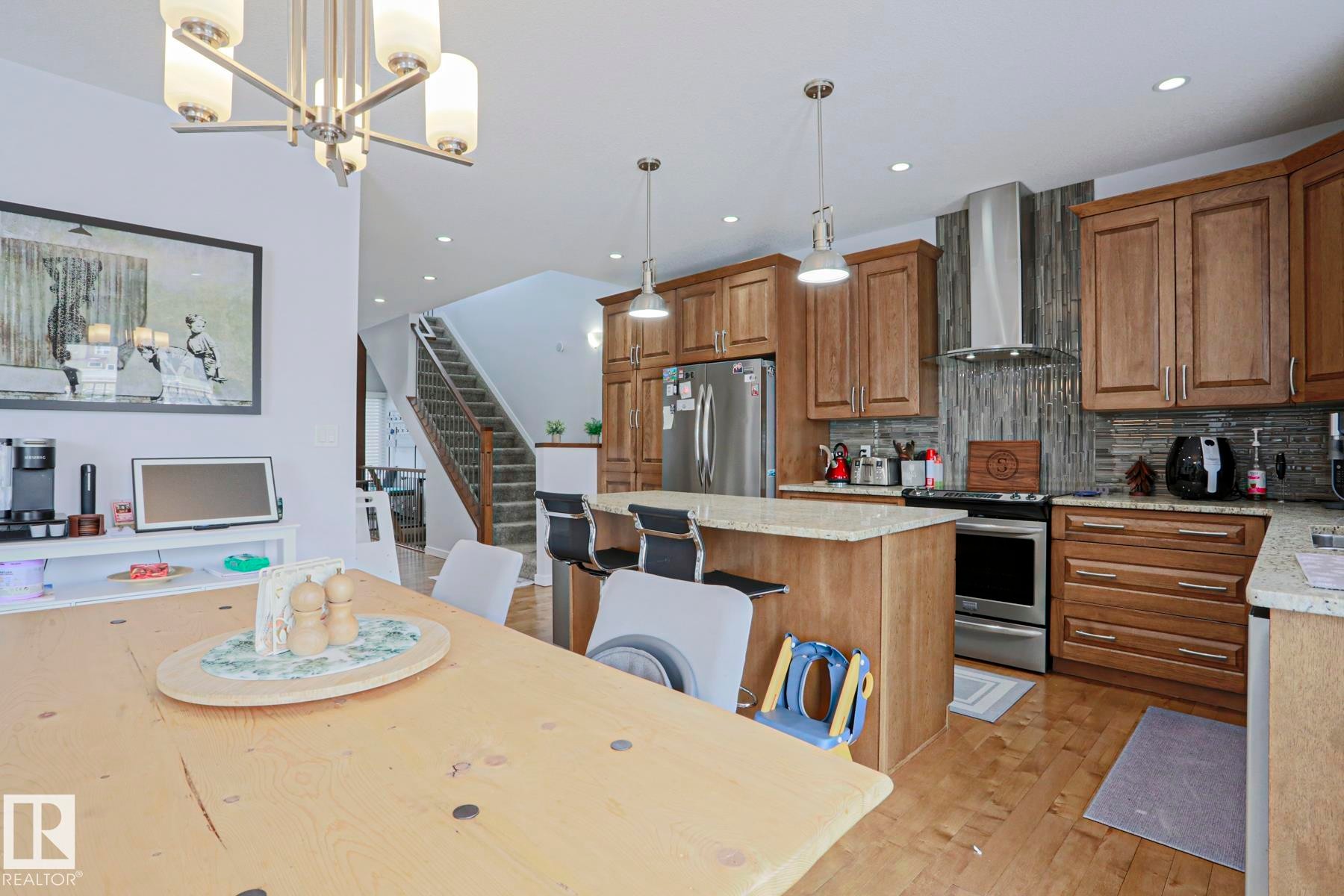 Bright kitchen and dining area featuring hardwood flooring, recessed lighting, and a kitchen island with seating - 18 Enchanted Way, St. Albert, AB