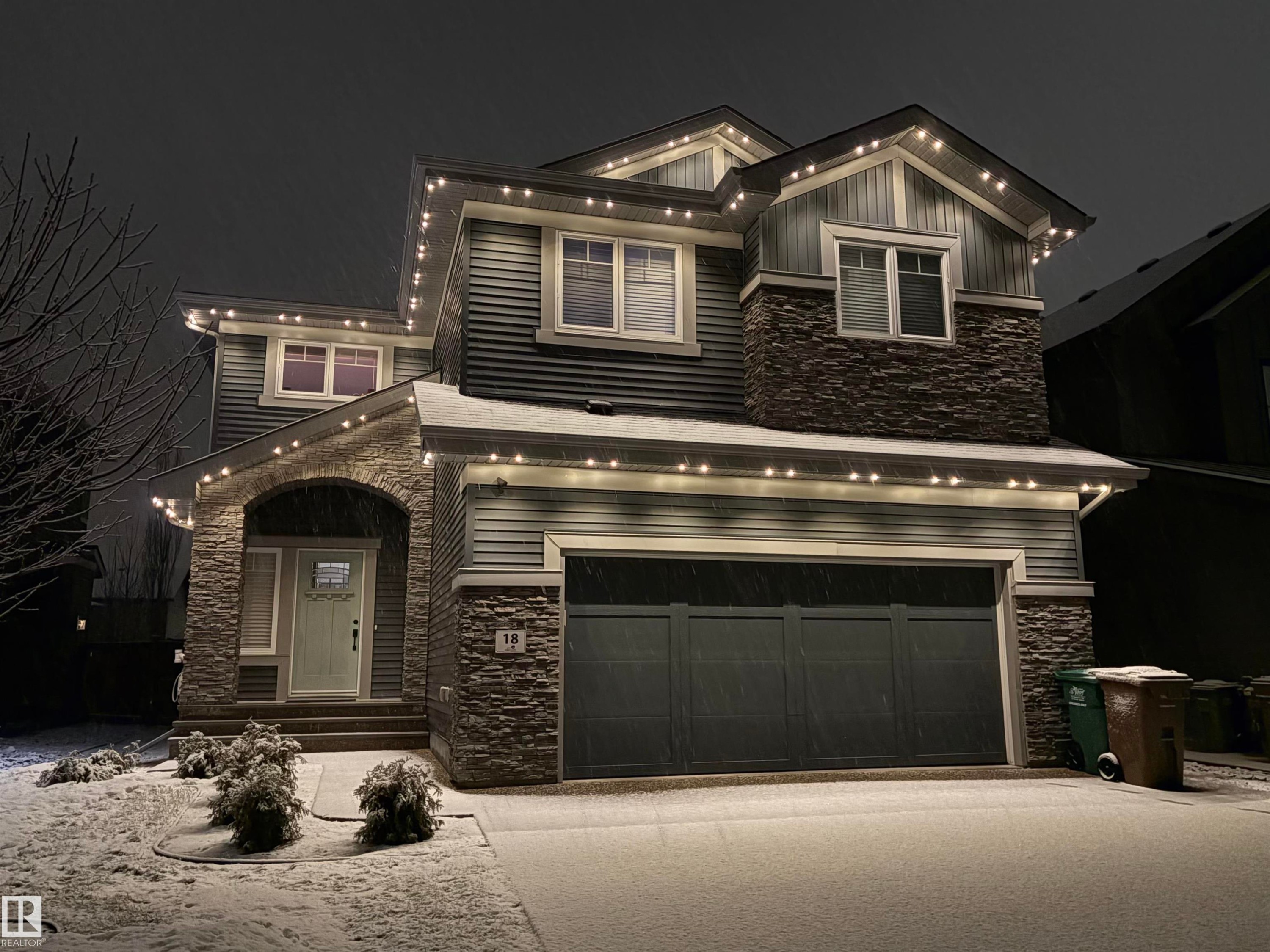 The property features a dark gray exterior with stone accents and a two-car garage - 18 Enchanted Way, St. Albert, AB