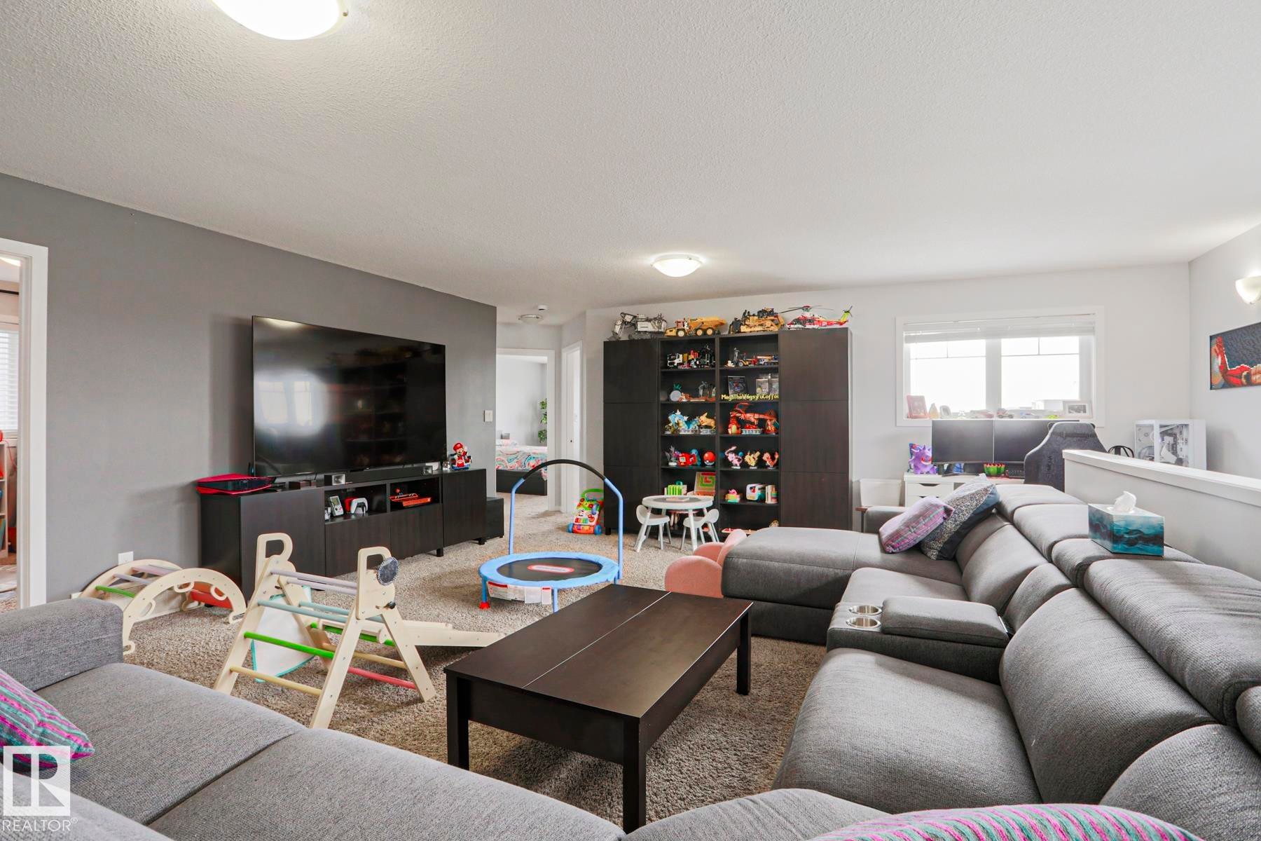 Spacious living area featuring neutral-toned carpeting, light-colored walls, and a large window providing natural light - 18 Enchanted Way, St. Albert, AB