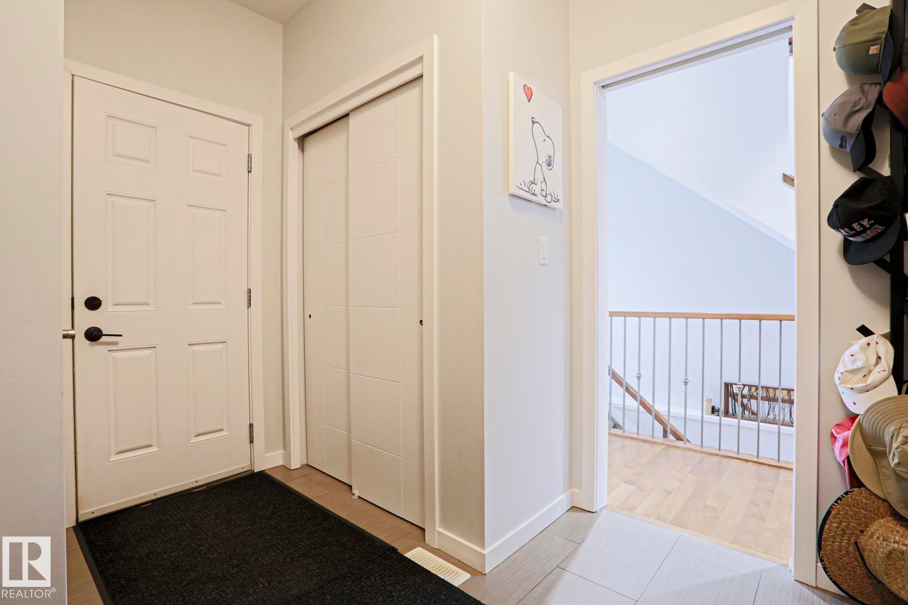 The foyer features a white paneled door with matte black hardware, a closet with sliding paneled doors, and light-colored flooring - 18 Enchanted Way, St. Albert, AB