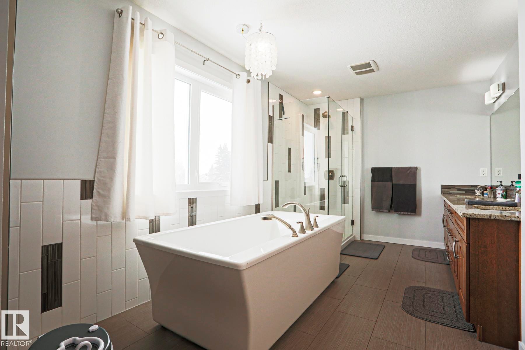 The bathroom features a freestanding tub, a glass-enclosed shower, a vanity with a granite countertop, and tiled floors - 18 Enchanted Way, St. Albert, AB