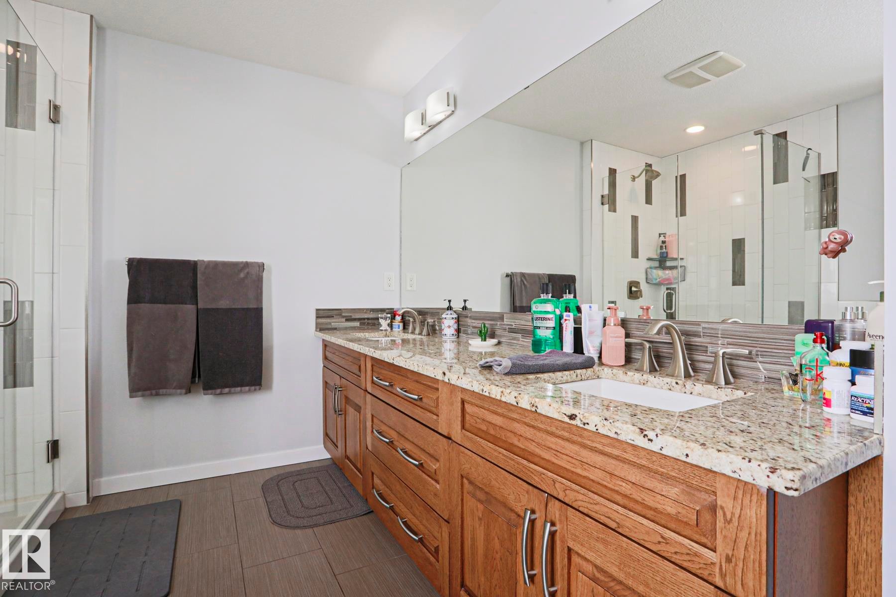 This bathroom features a double vanity with a light-colored granite countertop and a wood-toned cabinet - 18 Enchanted Way, St. Albert, AB