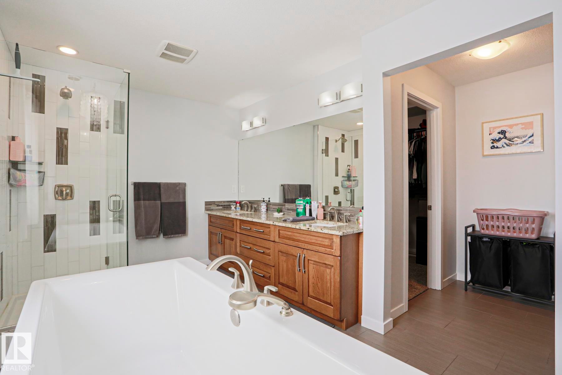 Well-appointed bathroom featuring a soaking tub, a walk-in shower with a glass enclosure and tiled walls, a vanity with a granite countertop and dual sinks, and light-colored flooring - 18 Enchanted Way, St. Albert, AB