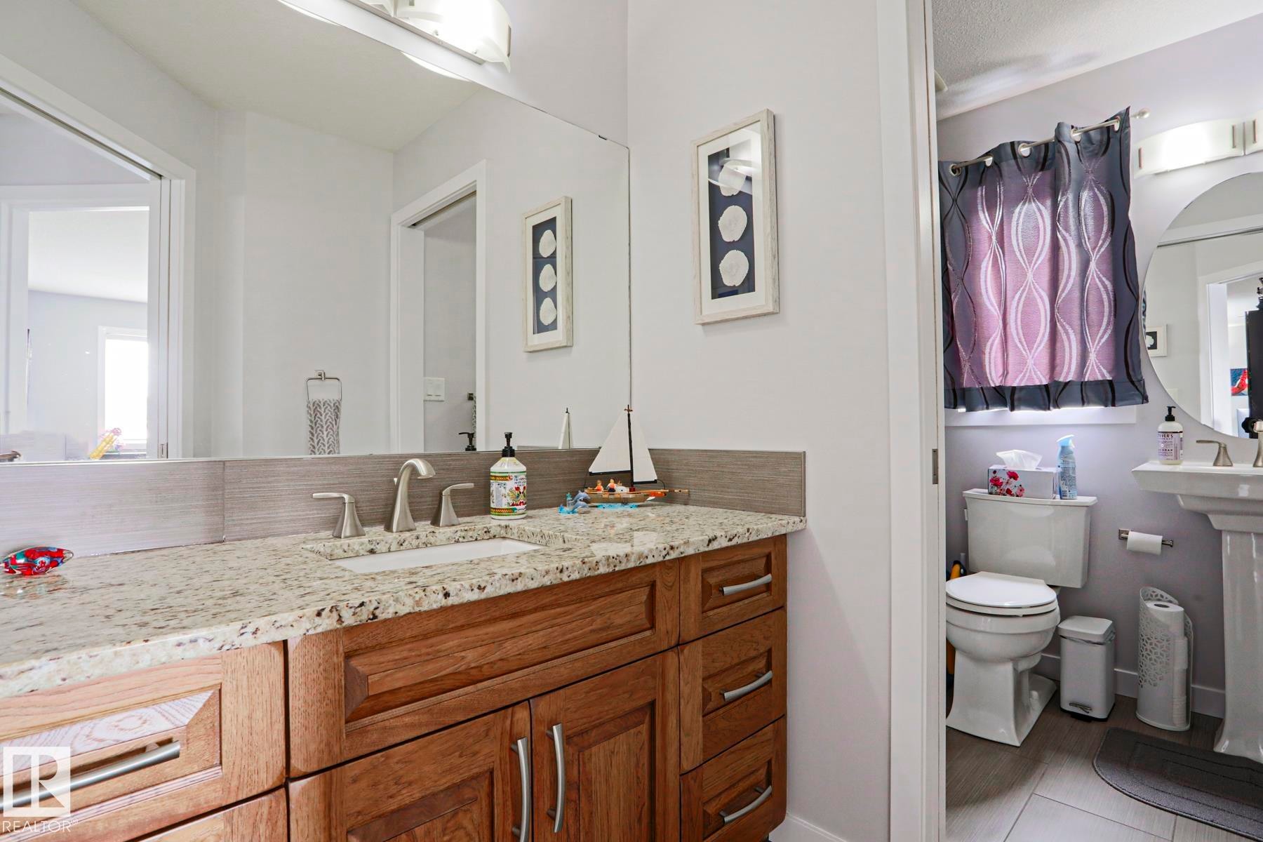 This bathroom features a vanity with a granite countertop, an undermount sink, and wood cabinetry - 18 Enchanted Way, St. Albert, AB
