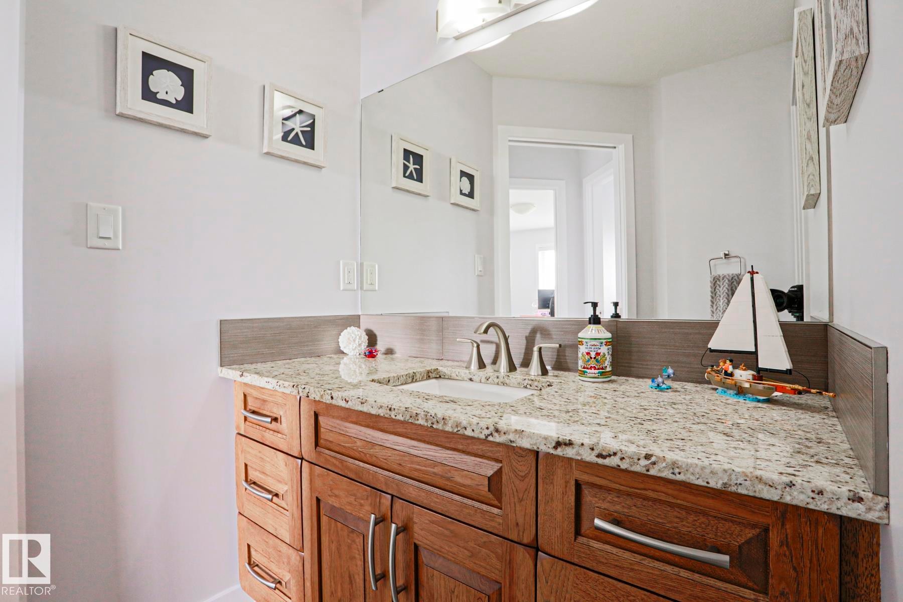 Bathroom featuring a vanity with a light granite countertop, a single sink, and wood cabinetry with brushed nickel hardware - 18 Enchanted Way, St. Albert, AB