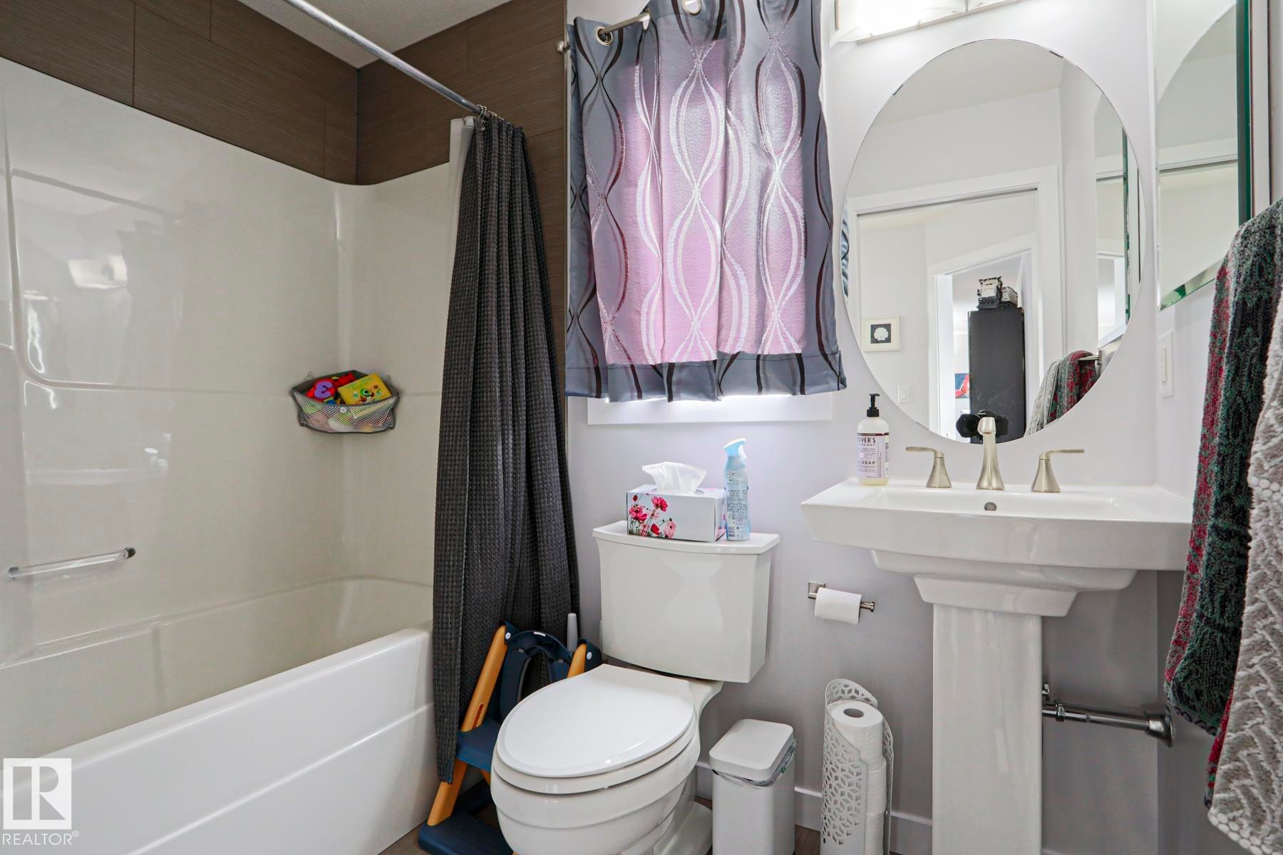 The bathroom features a white pedestal sink with a contemporary faucet, a toilet, and a bathtub with a shower - 18 Enchanted Way, St. Albert, AB