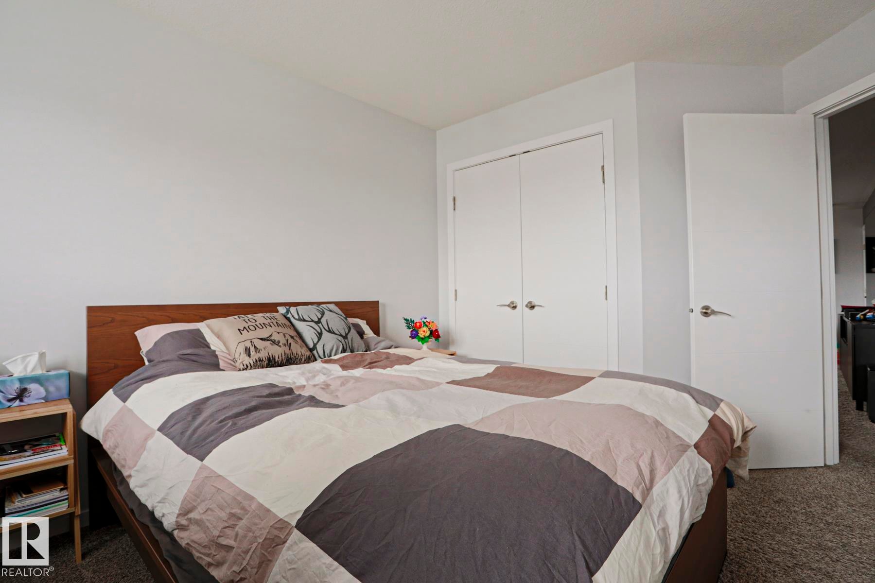 This bedroom features light-colored walls, carpet flooring, a wooden bed frame, and white closet doors with silver handles - 18 Enchanted Way, St. Albert, AB