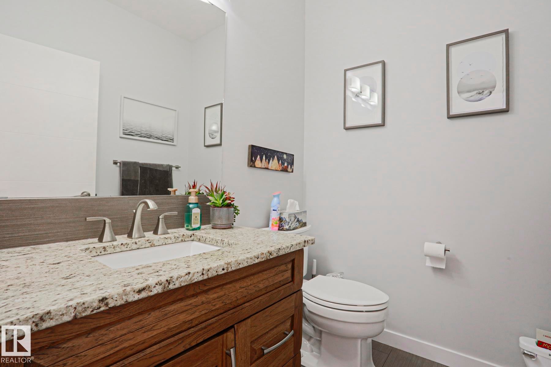 Bathroom featuring a white toilet, a wooden vanity with granite countertops, and a rectangular sink with a brushed nickel faucet - 18 Enchanted Way, St. Albert, AB