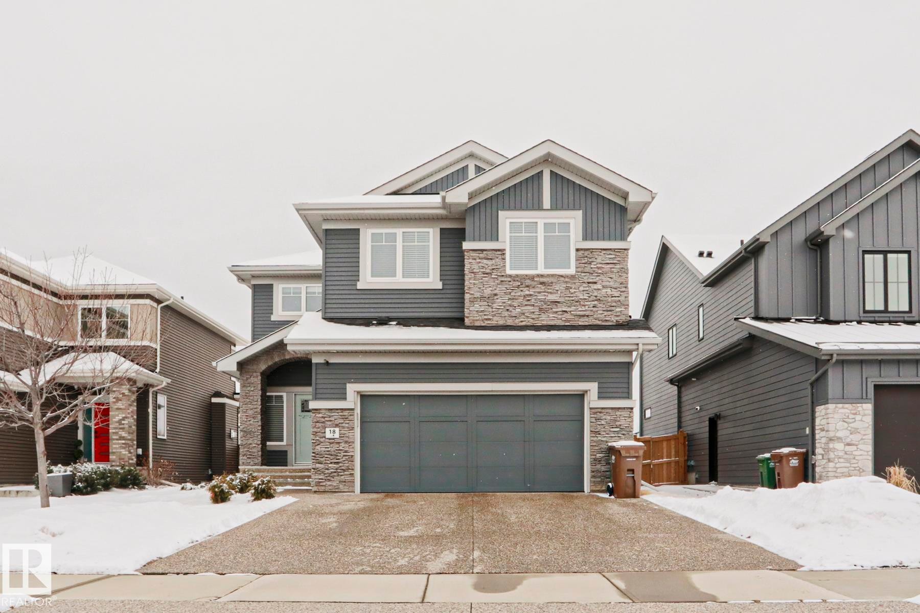 The property features a two-story exterior with grey siding and stone accents, a double garage, and a covered entryway - 18 Enchanted Way, St. Albert, AB