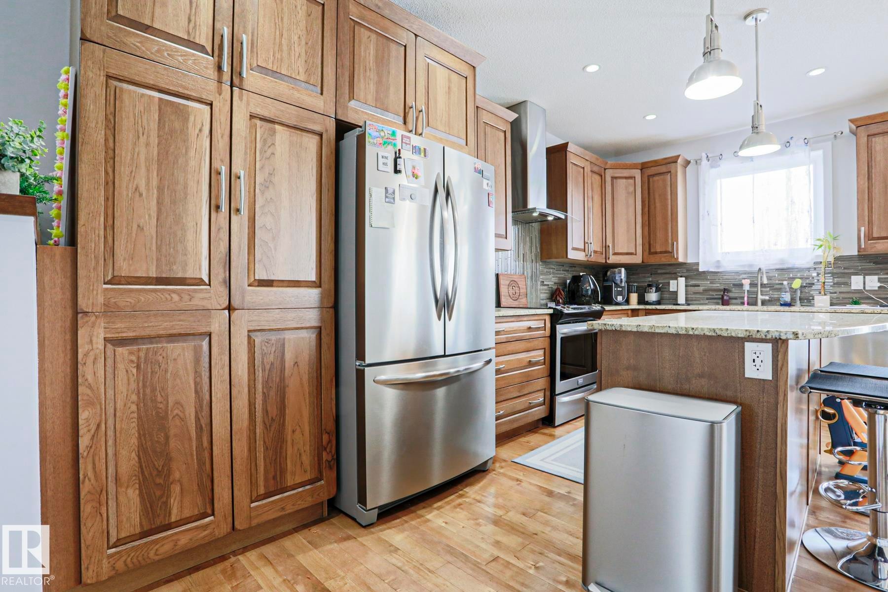The kitchen features wood cabinetry, stainless steel appliances, and hardwood floors - 18 Enchanted Way, St. Albert, AB