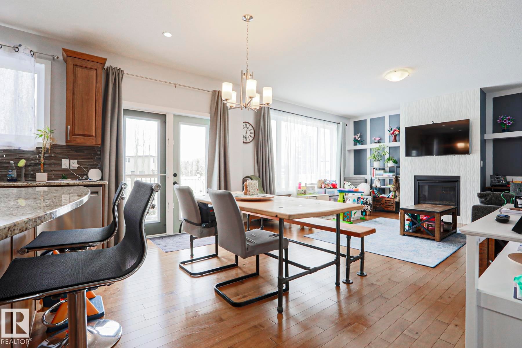 The open-concept living area features hardwood flooring, an island with granite countertops, and a fireplace with built-in shelving - 18 Enchanted Way, St. Albert, AB