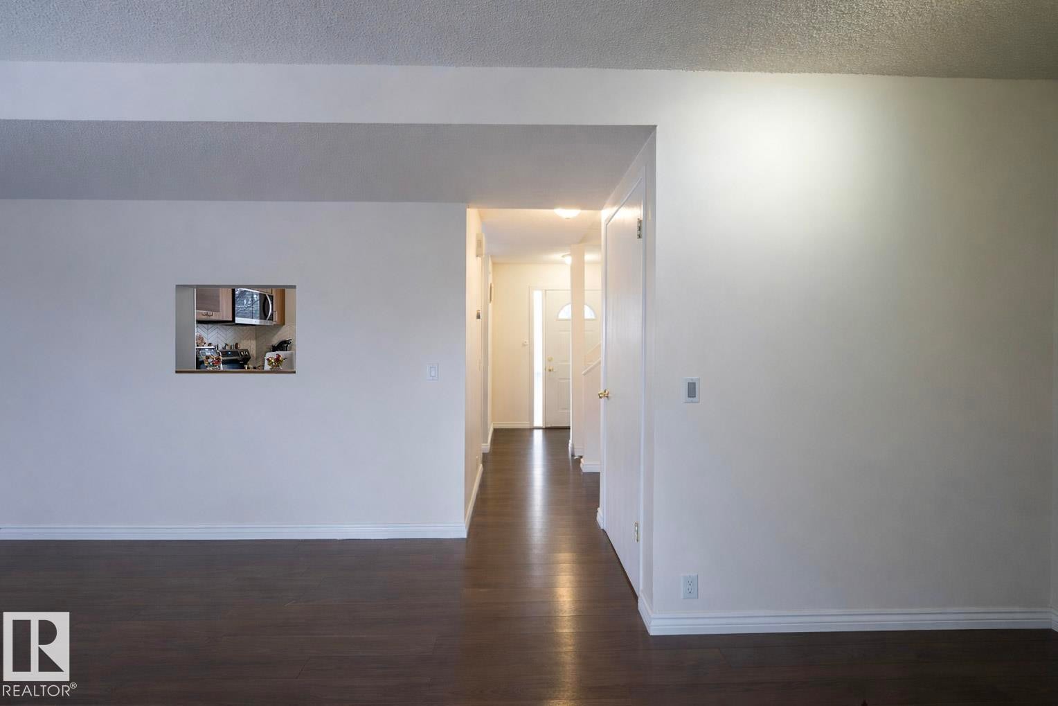 This interior space features dark wood flooring, white walls, and a pass-through window to the kitchen - 1728 37 Street, Edmonton, AB - Indoor Photo Showing Other Room