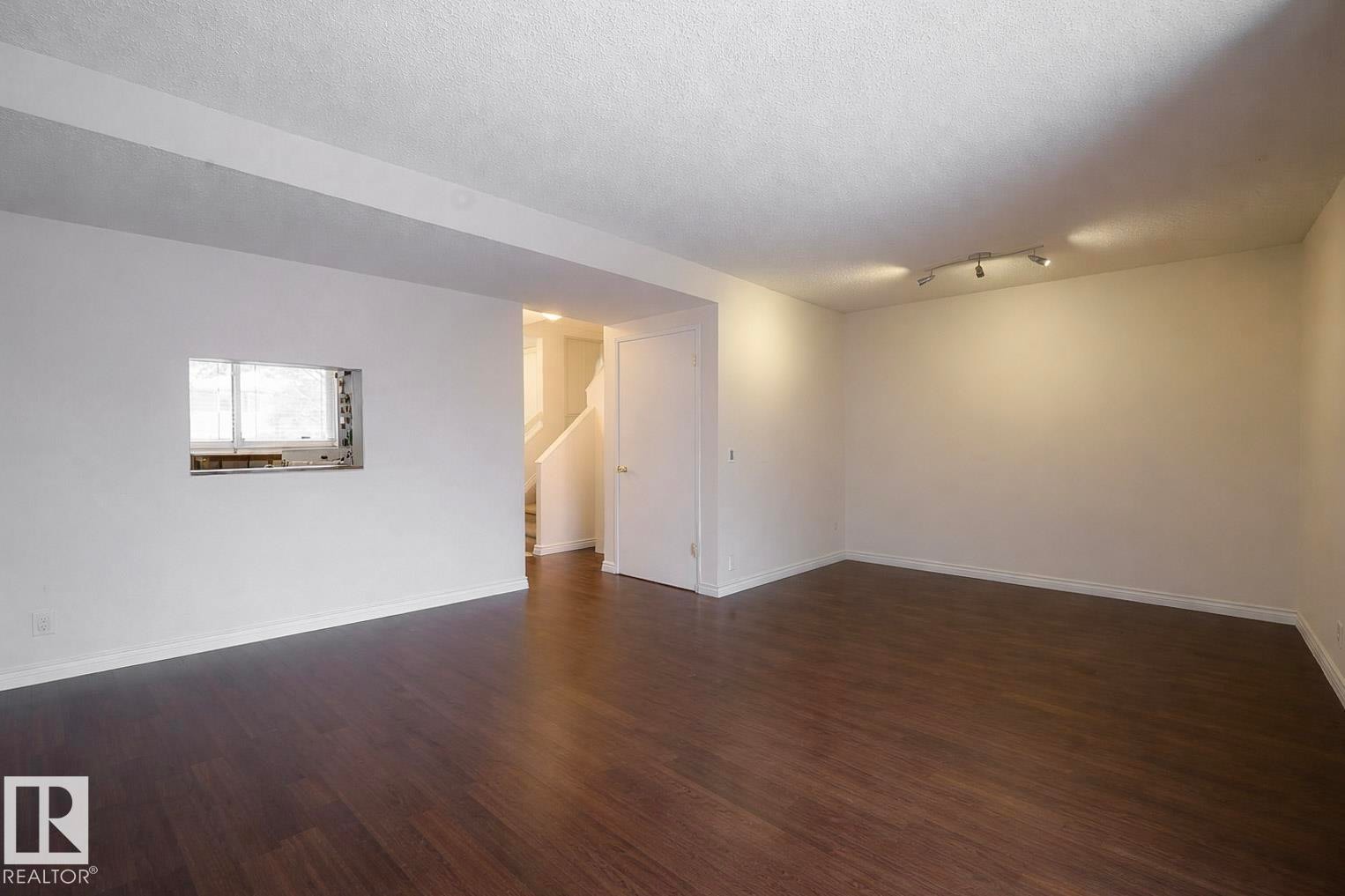Spacious interior room with dark wood flooring, white walls, and a track lighting fixture on the ceiling - 1728 37 Street, Edmonton, AB - Indoor Photo Showing Other Room