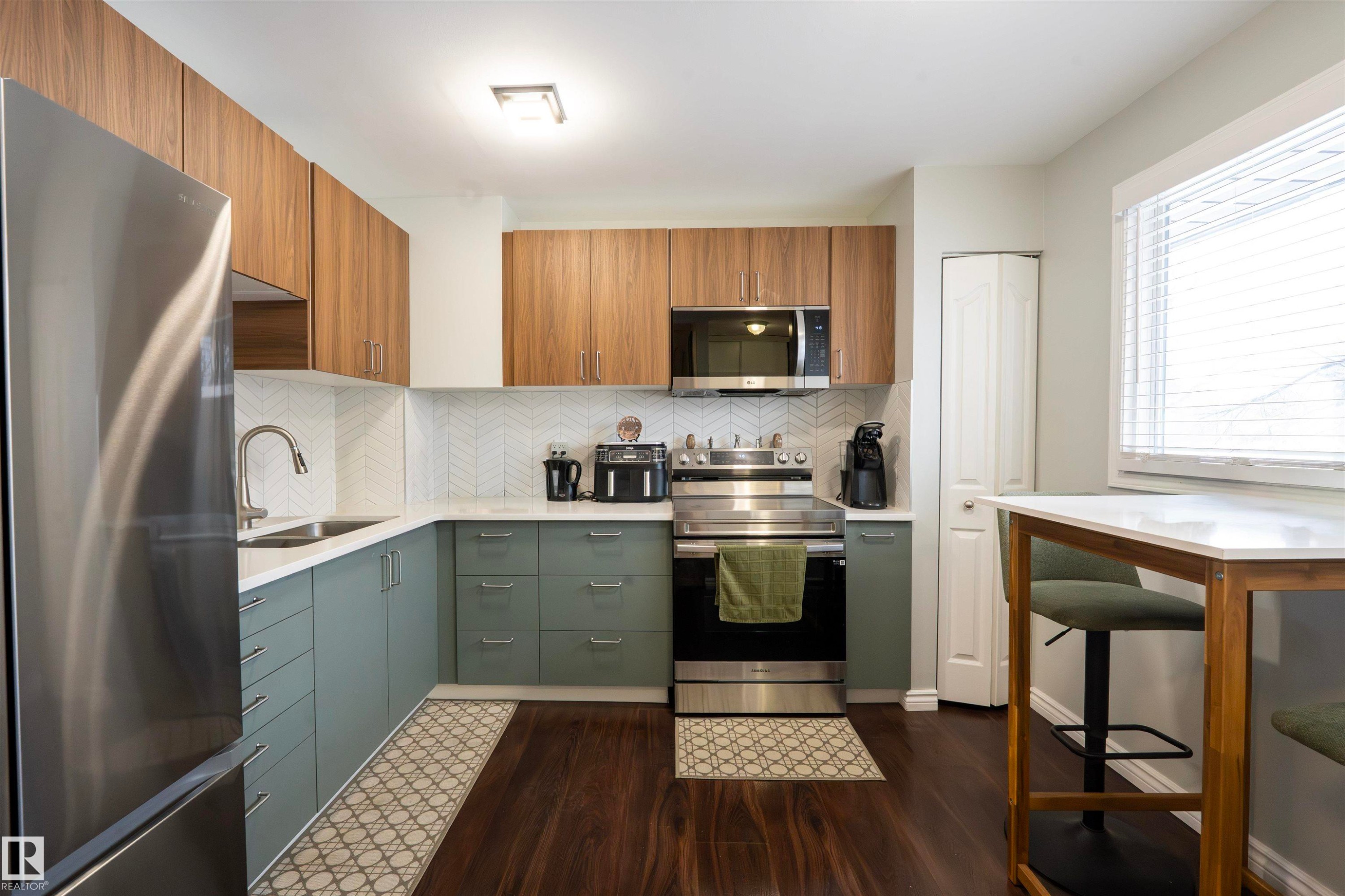 The kitchen features stainless steel appliances, wood-toned upper cabinetry, and contrasting green lower cabinetry - 1728 37 Street, Edmonton, AB - Indoor Photo Showing Kitchen With Double Sink With Upgraded Kitchen