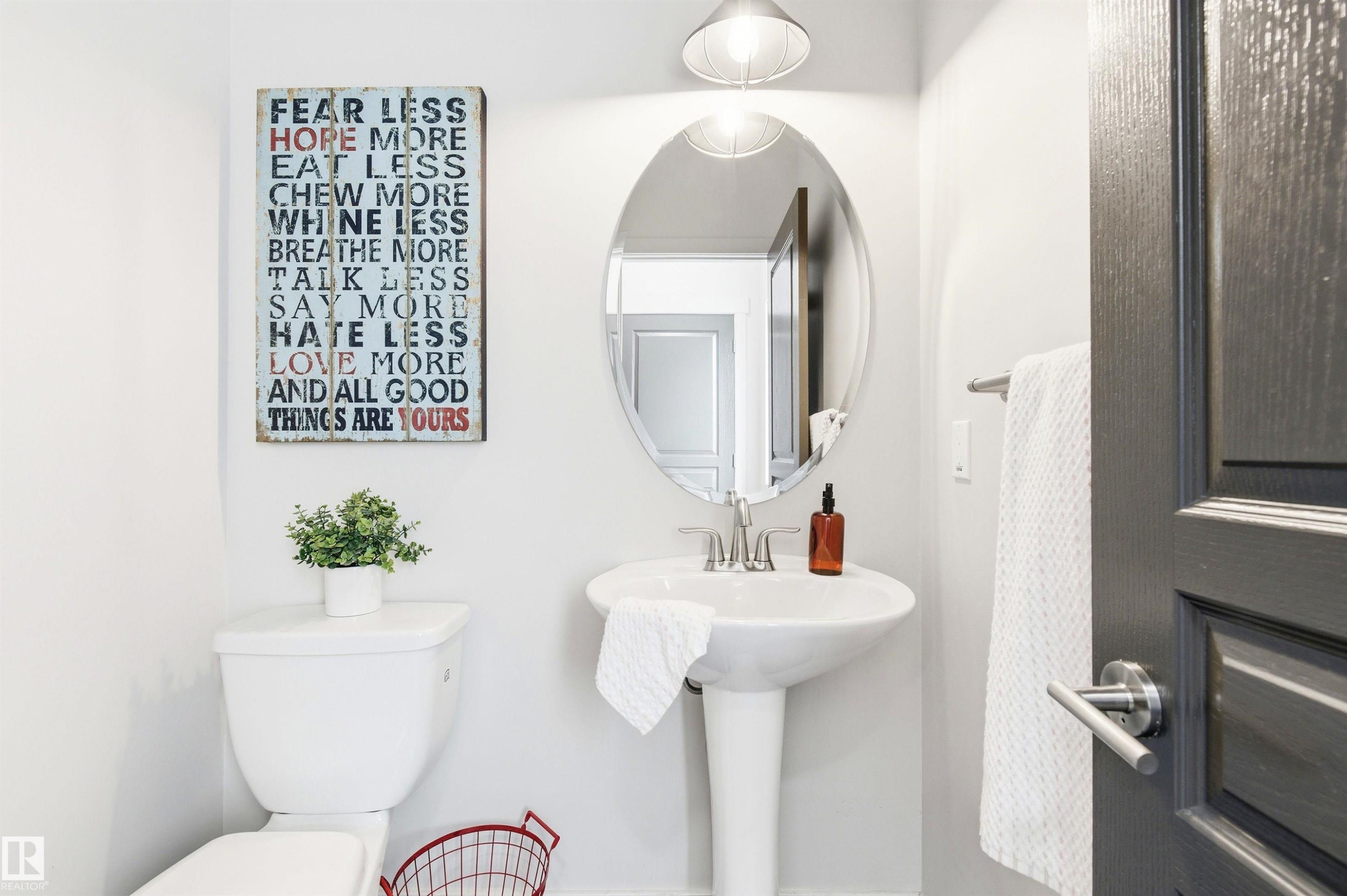 This bathroom features a pedestal sink with a contemporary faucet, an oval mirror, and a white toilet - 678 Secord Boulevard, Edmonton, AB - Indoor Photo Showing Bathroom