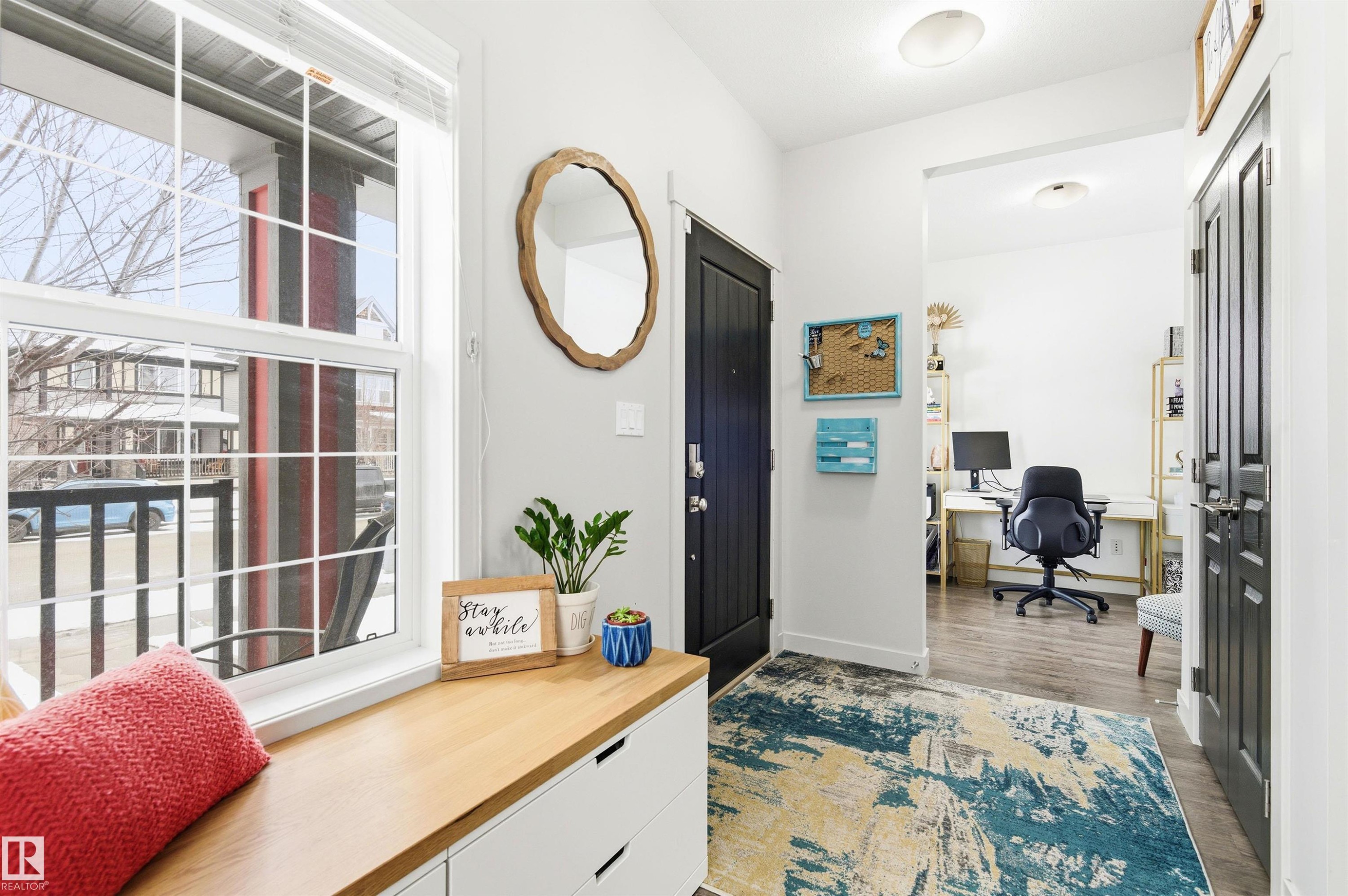 Entryway featuring a window with white blinds, a wooden bench with drawers, and a dark paneled door - 678 Secord Boulevard, Edmonton, AB - Indoor Photo Showing Other Room
