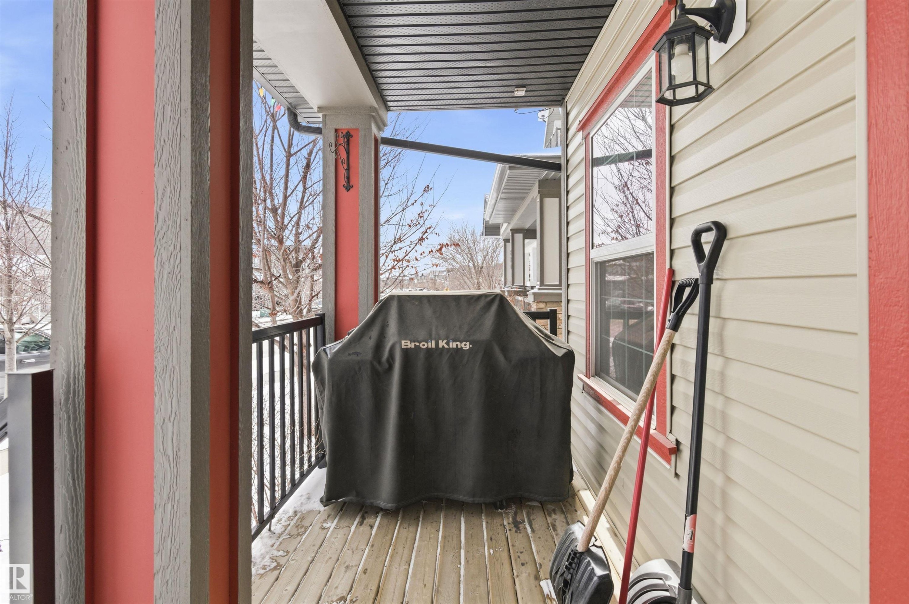 This property features a covered balcony with wood-planked flooring, a black metal railing, and an outdoor wall lantern - 678 Secord Boulevard, Edmonton, AB - With Exterior
