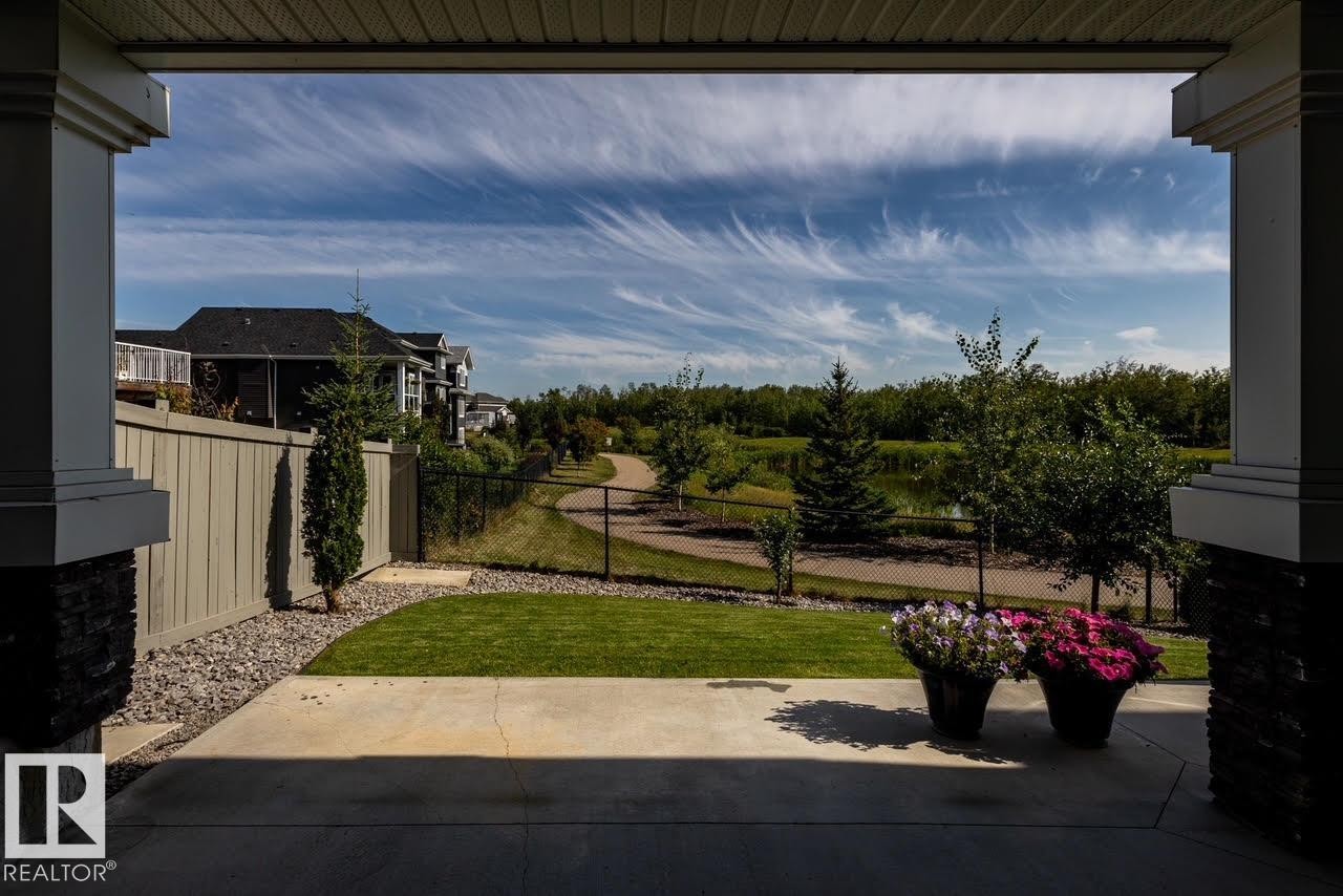 Concrete patio area with stone pillar accents, manicured lawn, and a light-colored privacy fence - 3419 Chickadee Drive, Edmonton, AB - Outdoor