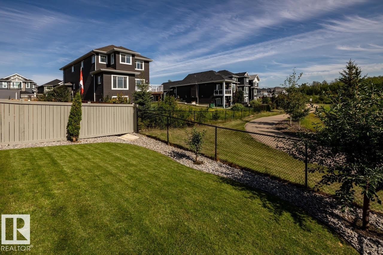 Expansive backyard featuring a manicured lawn, full-height privacy fencing, and a black chain-link fence bordering a paved pathway - 3419 Chickadee Drive, Edmonton, AB - Outdoor