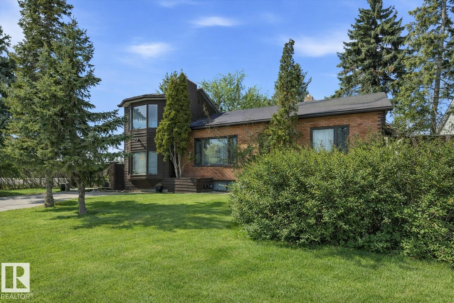 The property features a brick exterior, a bay window, and a well-maintained lawn with mature trees and shrubs/ This is a summer picture using AI - 11026 110 Avenue, Edmonton, AB - Outdoor