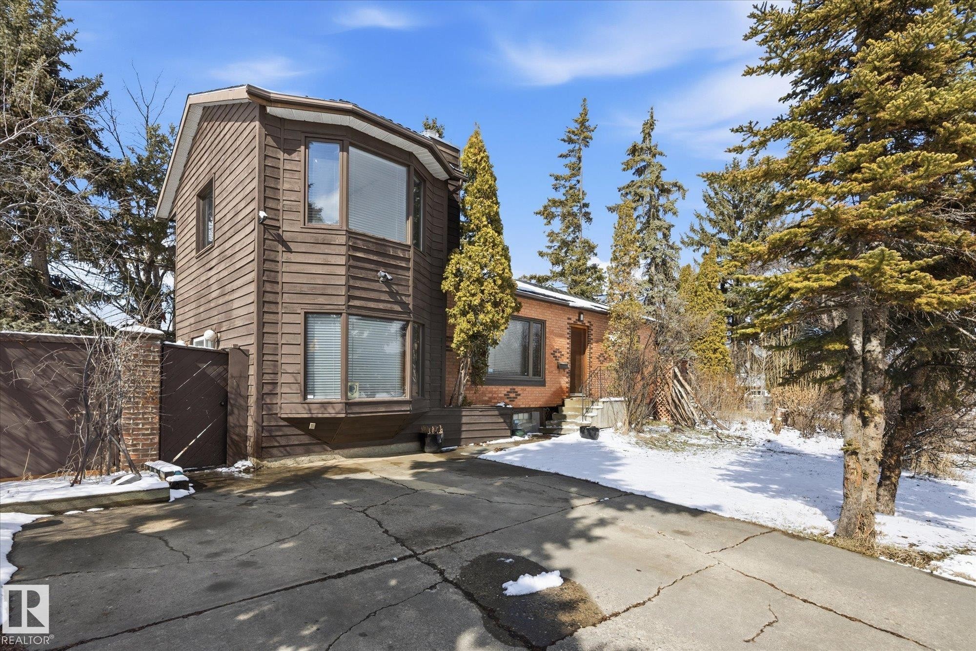 Exterior view of the property featuring a brown wood-sided section with large bay windows, a brick section with a covered entrance, and a paved driveway - 11026 110 Avenue, Edmonton, AB - Outdoor