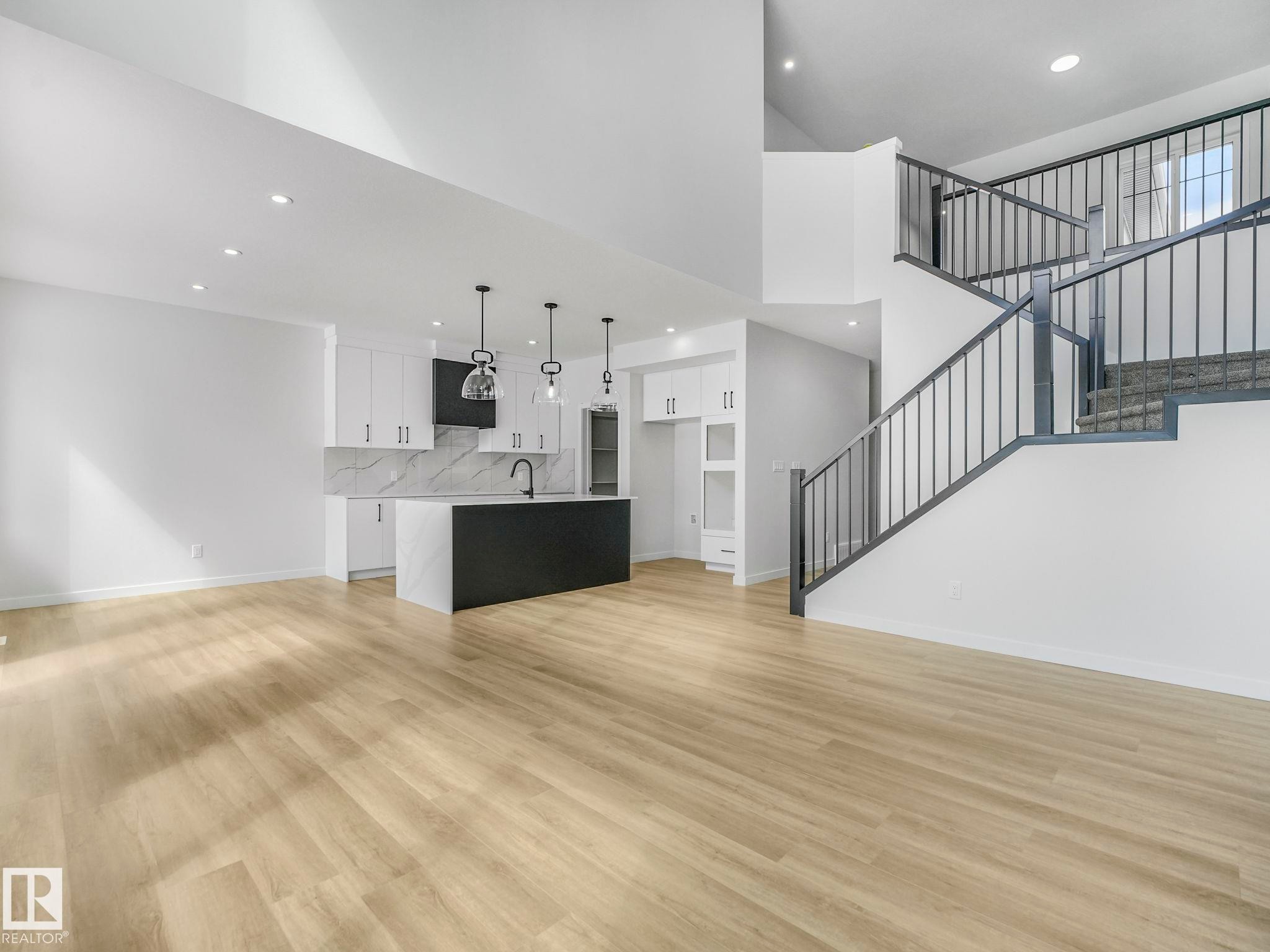 The open concept living area features light-toned flooring, recessed lighting, and a kitchen with white cabinetry, a dark island, and pendant lighting - 239 Kinglet Boulevard Nw, Edmonton, AB - Indoor Photo Showing Kitchen