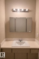 Bathroom vanity featuring a light-colored countertop, an integrated sink, and a tri-fold medicine cabinet, illuminated by a four-bulb light fixture -