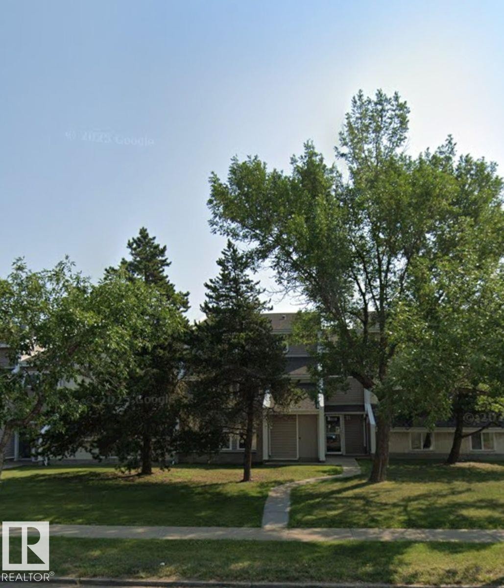 The property features a multi-story building with a light-colored facade, dark roof, and prominent entryway - 4 3819 76 Street, Edmonton, AB - Outdoor