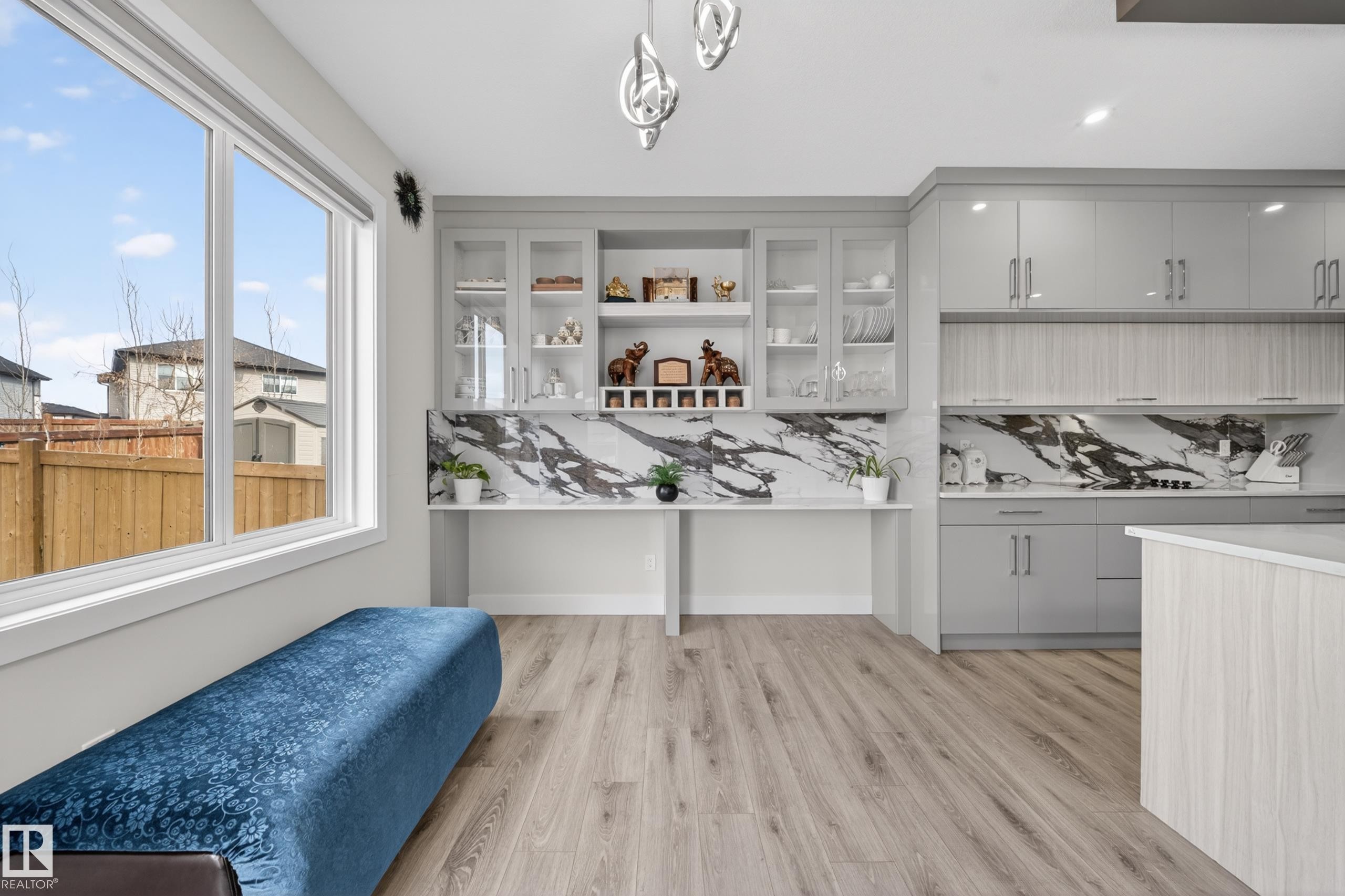This open-concept area features large windows, light wood-style flooring, a kitchen with grey cabinetry, and a built-in display unit with a marble-patterned backsplash - 449 Roberts Crescent, Leduc, AB - Indoor Photo Showing Kitchen
