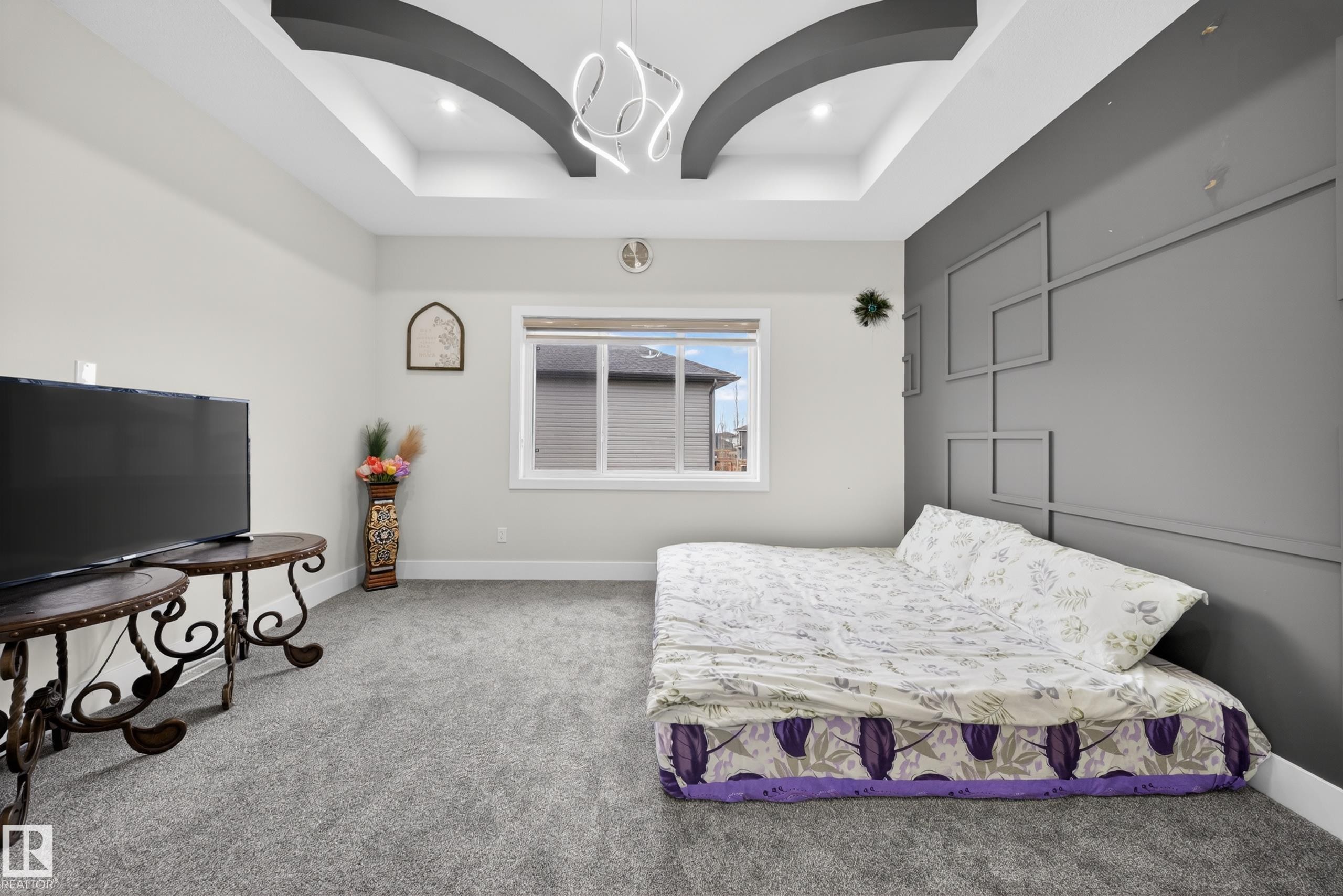 This room features a tray ceiling with a contemporary light fixture, plush grey carpeting, and a window providing natural light - 449 Roberts Crescent, Leduc, AB - Indoor Photo Showing Bedroom