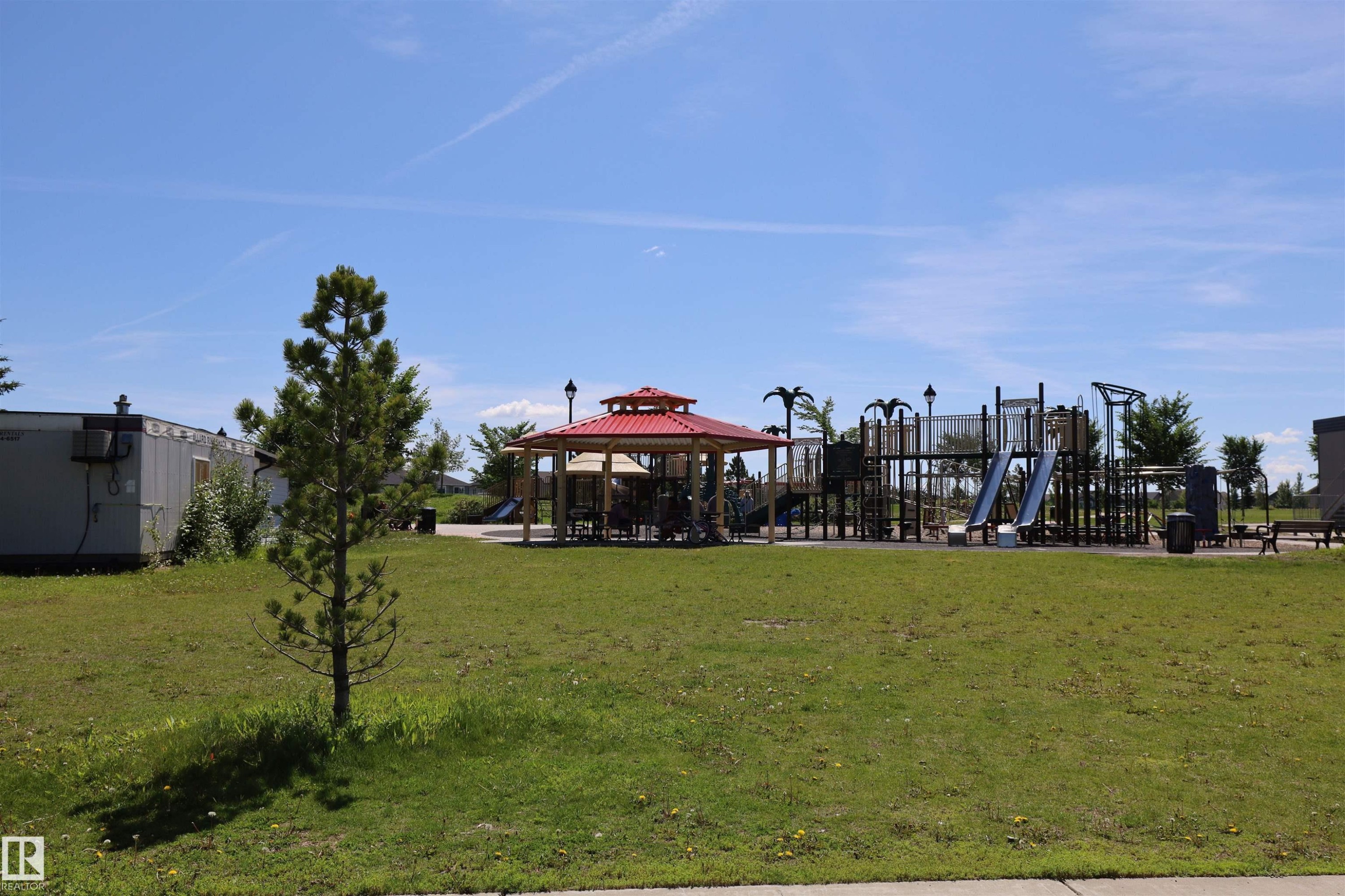 Community park area featuring a red-roofed gazebo, a comprehensive playground structure with slides, and an expansive grassy lawn - 4044 Alexander Way, Edmonton, AB