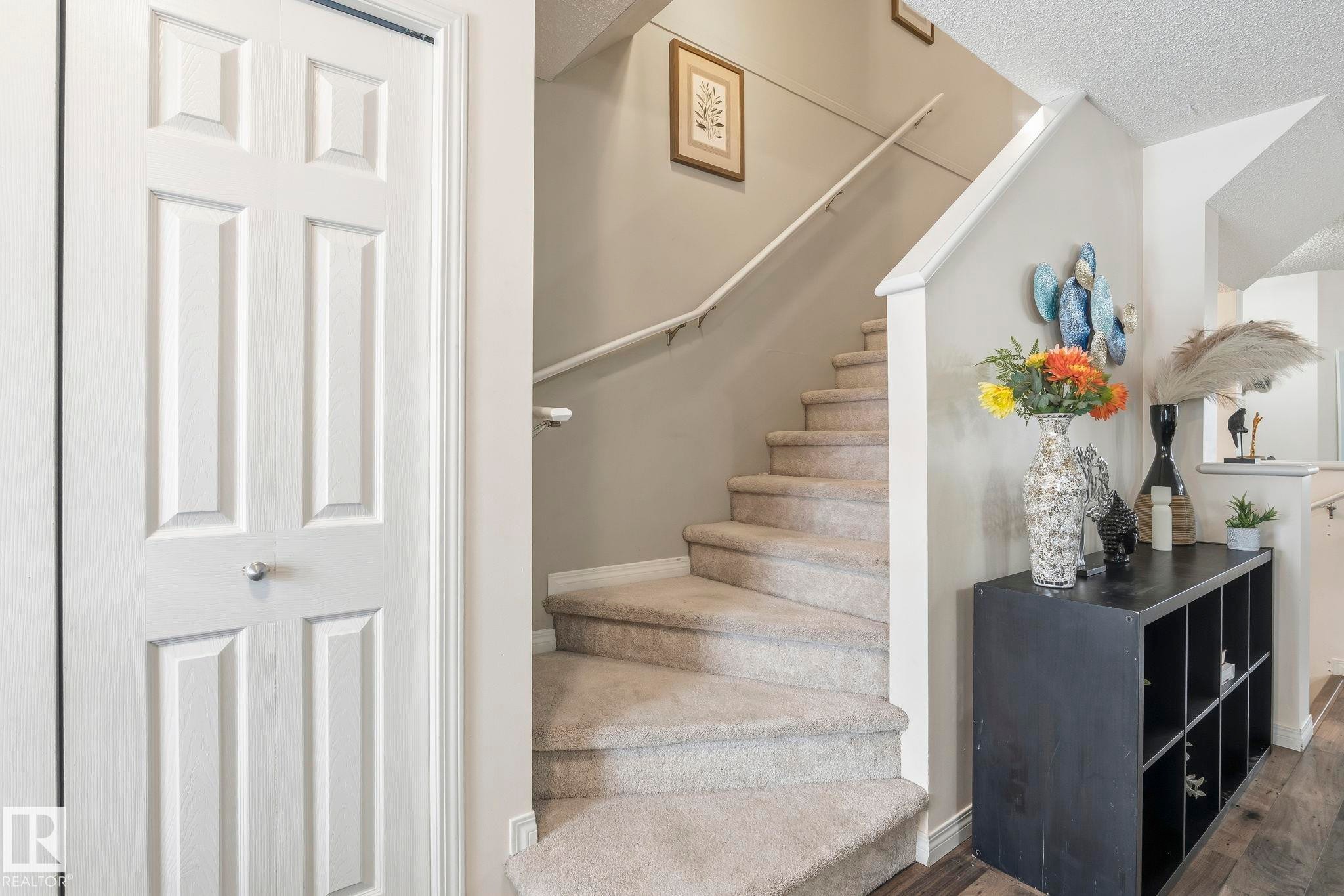 The property features a staircase with carpeted steps and a white railing, a white bi-fold door, and wood-style flooring - 4783 Crabapplle Run, Edmonton, AB - Indoor Photo Showing Other Room